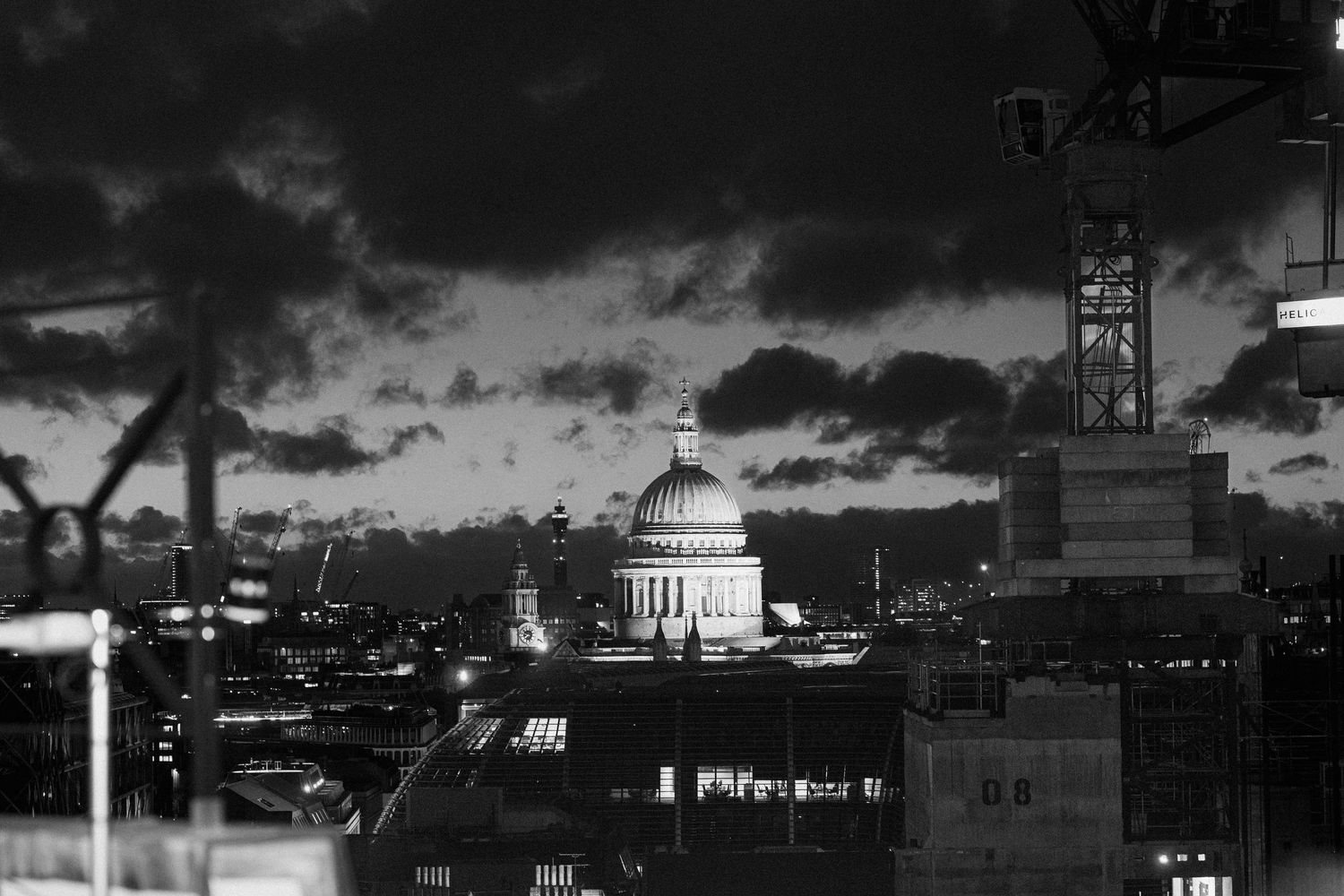 Dramatic black and white cityscape silhouette with dark stormy clouds overhead.