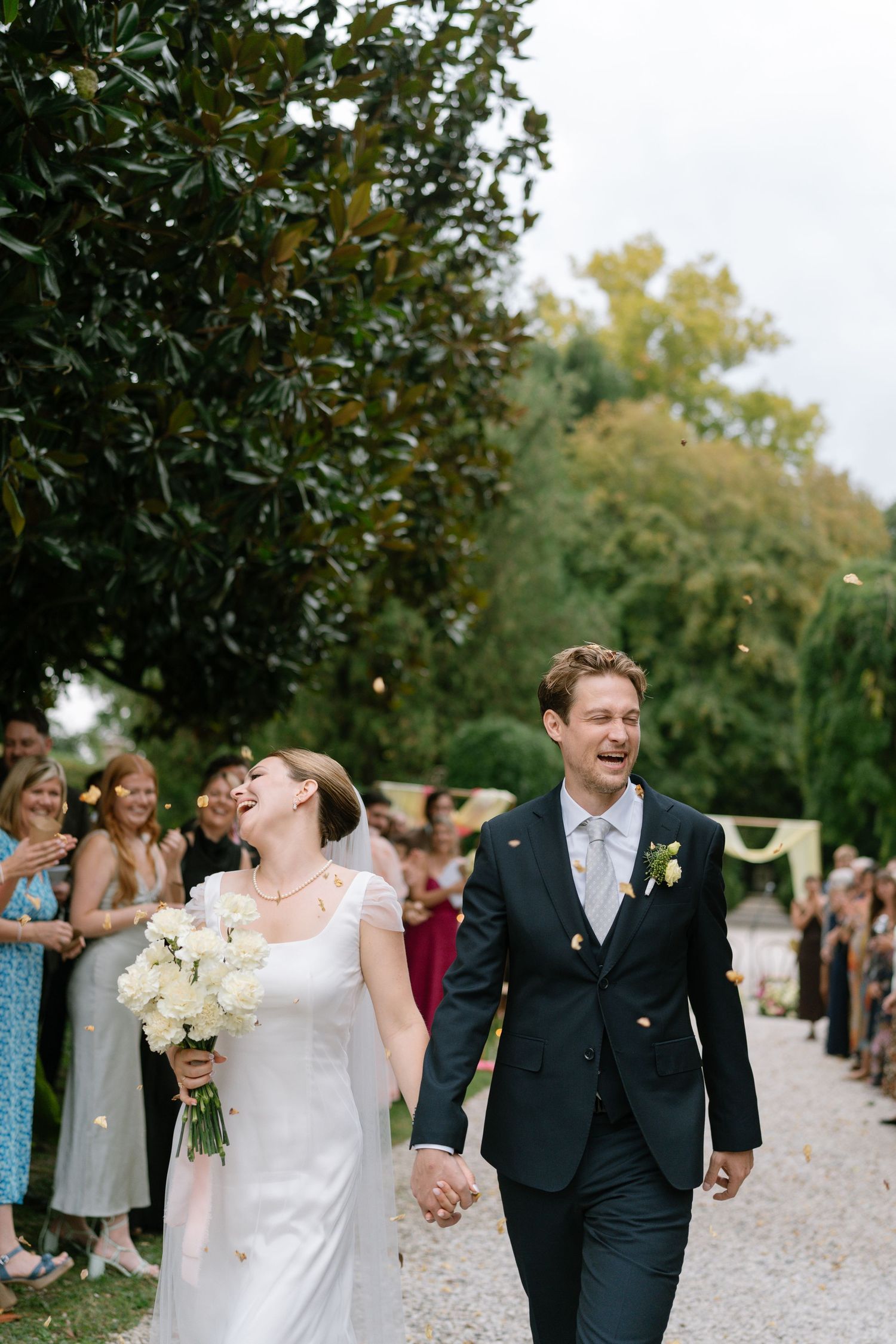 A couple walks hand in hand down a garden path while guests shower them with confetti.
