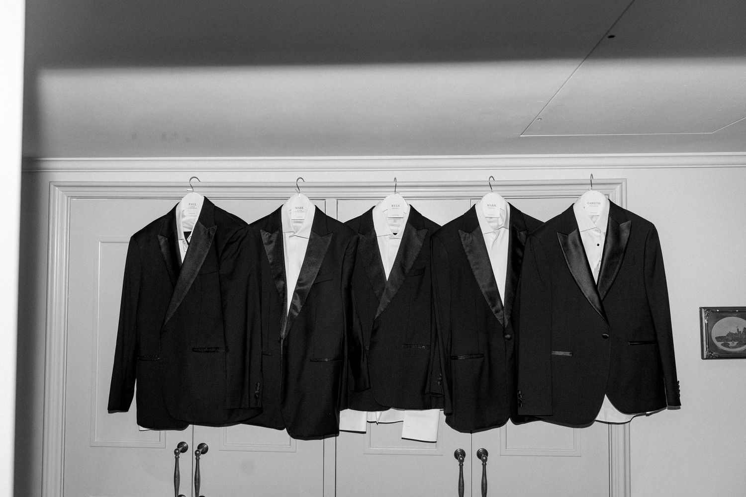 Row of black formal suits hanging neatly on white hangers against wall.