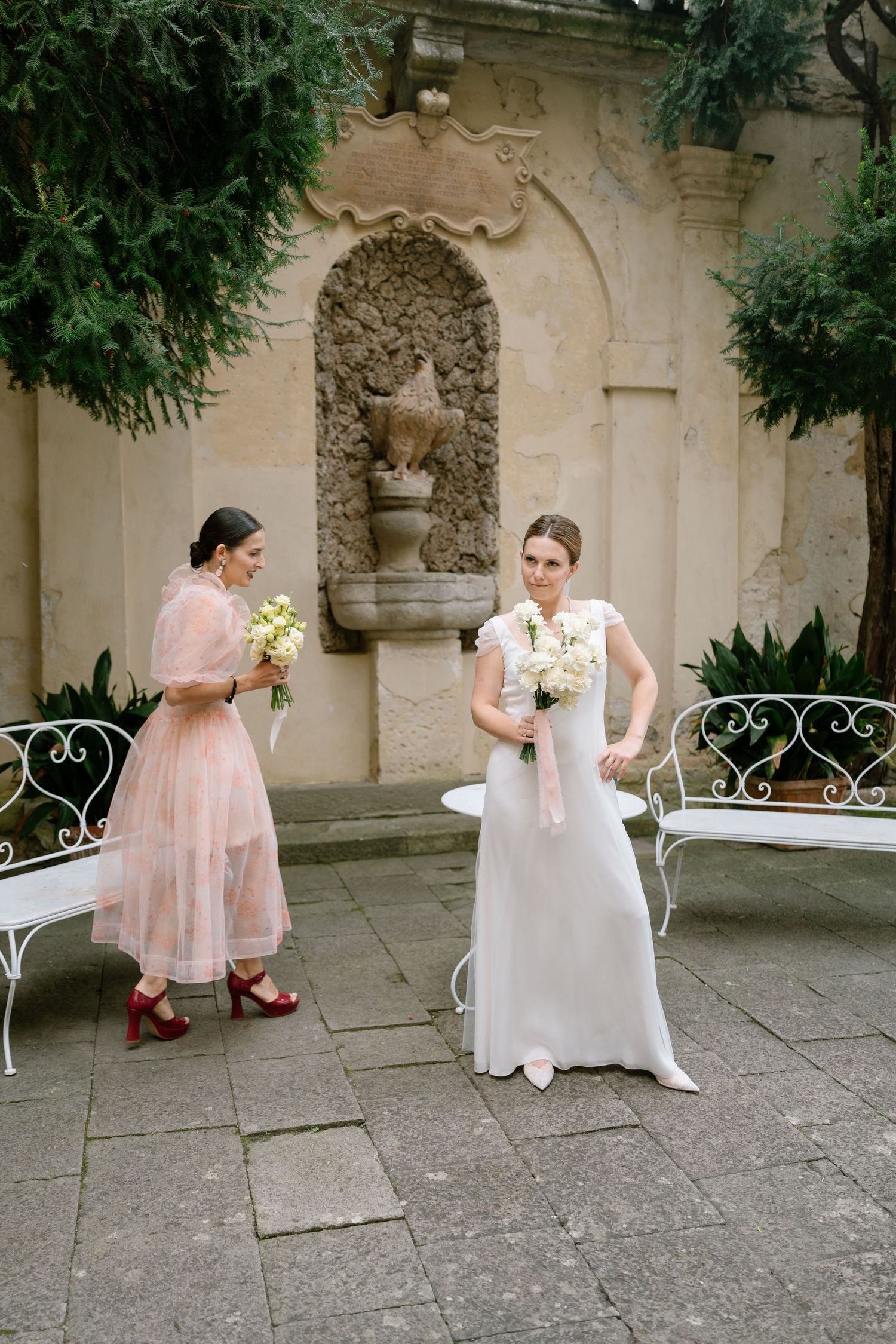 Wedding party relaxes on white garden furniture in an elegant stone courtyard.