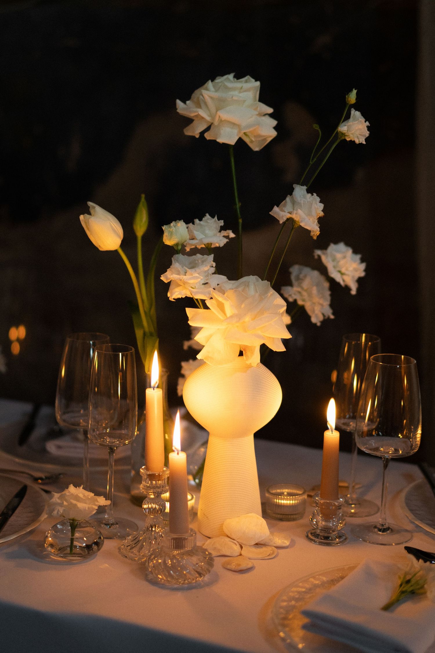 Elegant table setting with white flowers in frosted vase, wine glasses and glowing candles.