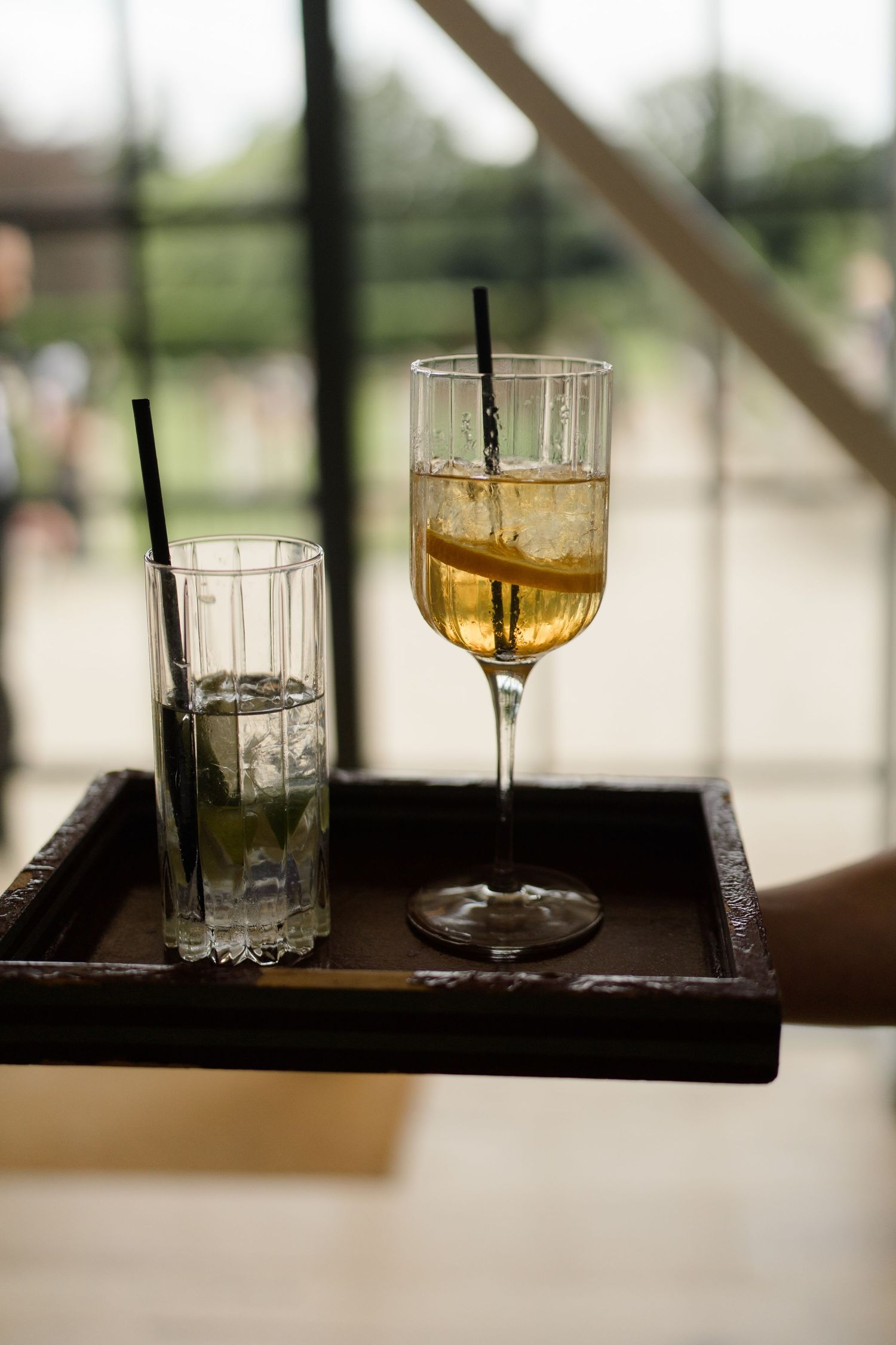 Two cocktails on wooden tray, one mojito and one wine glass with lemon slice, served at wedding.