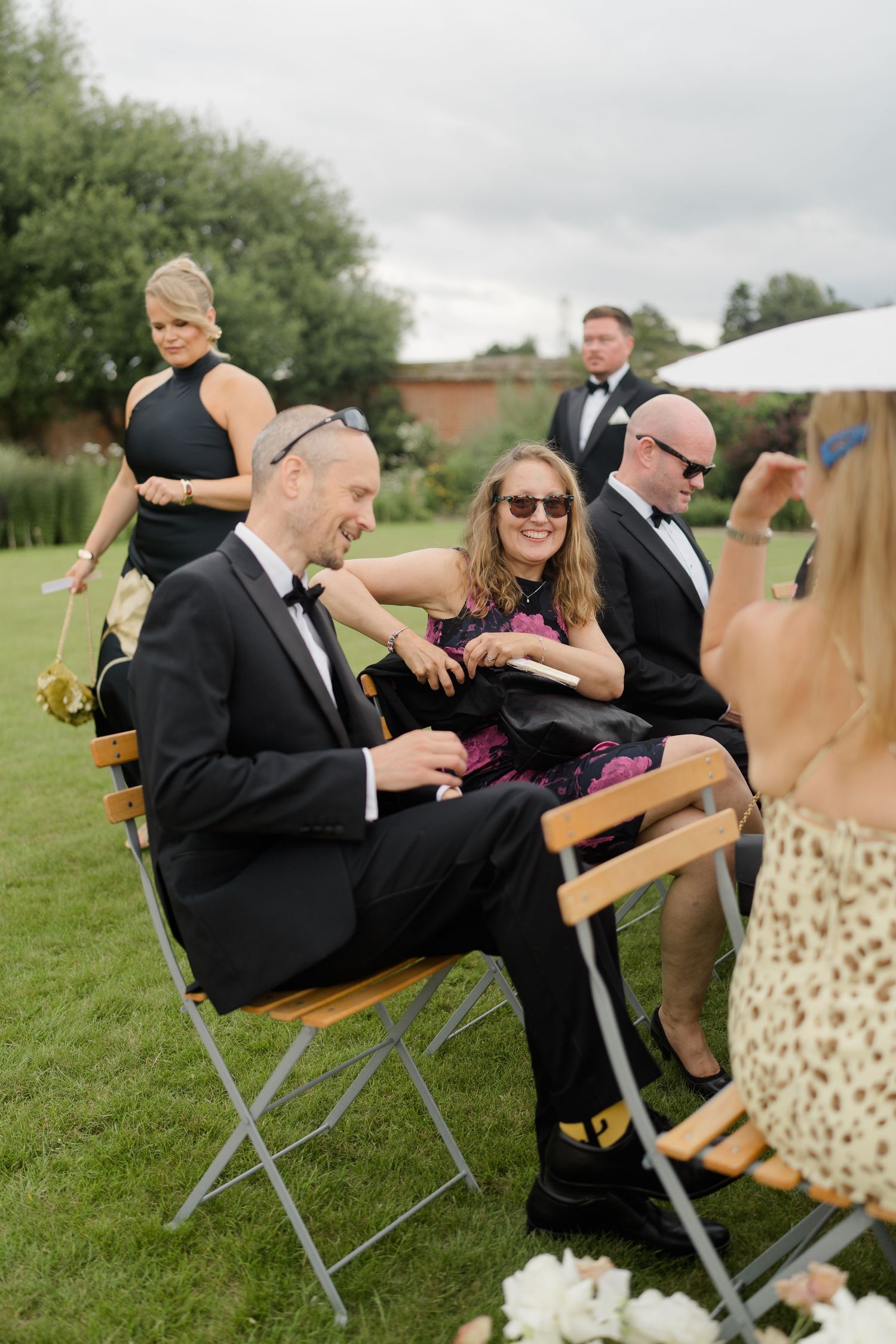 Wedding guests socializing outdoors at garden ceremony seating area.
