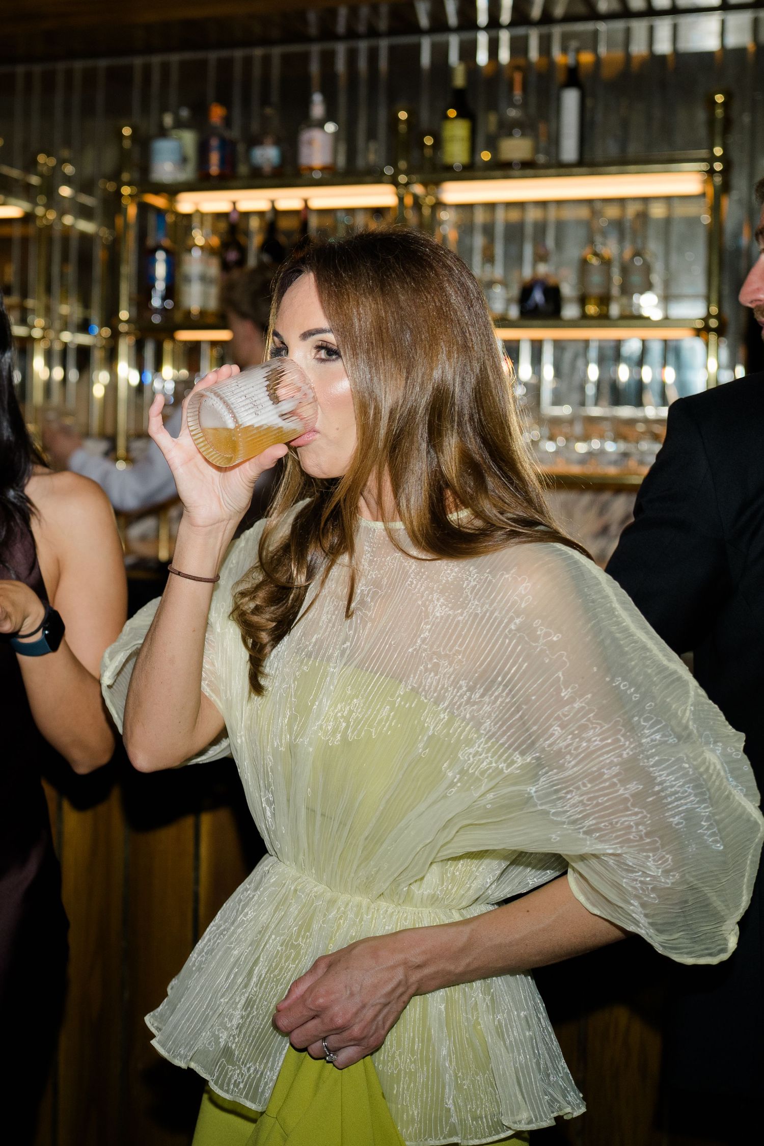 Wedding guest in yellow dress drinks champagne at elegant bar during reception.