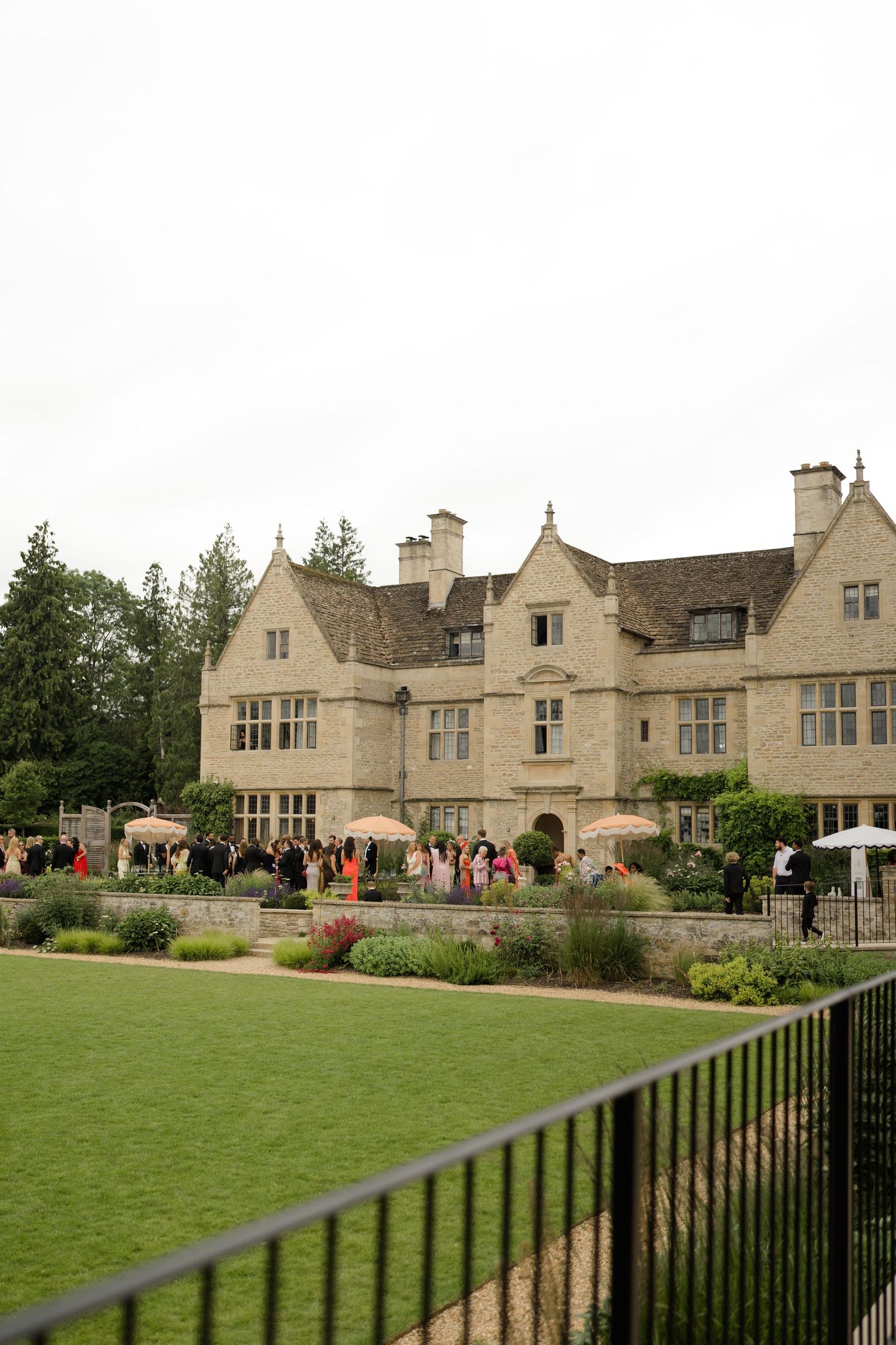 Guests mingling outside a grand Cotswolds stone manor house during a wedding reception.