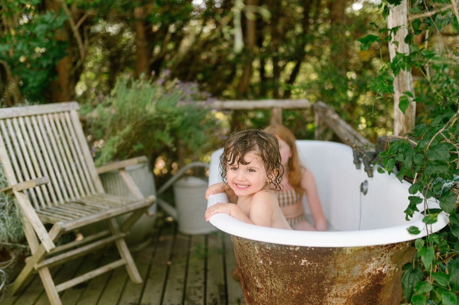 Outdoor bathtub scene surrounded by lush greenery and wooden furniture.