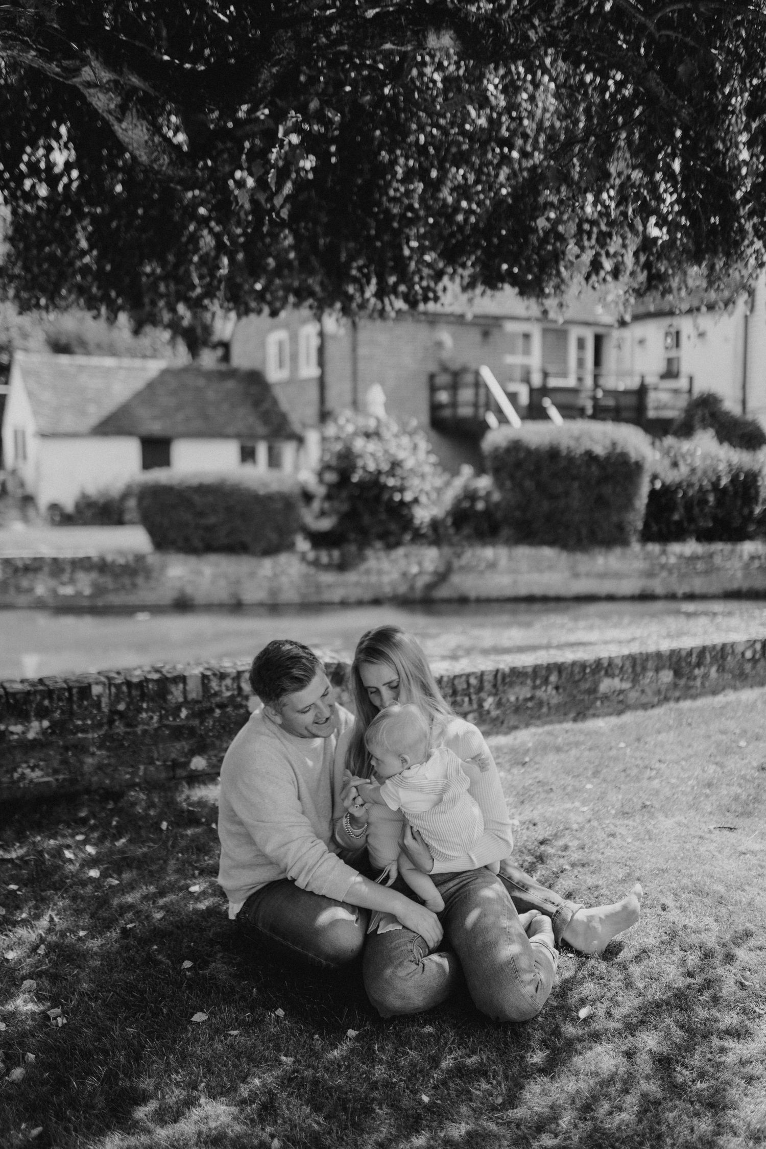 Two children playing together on grass under tree shade in black and white.