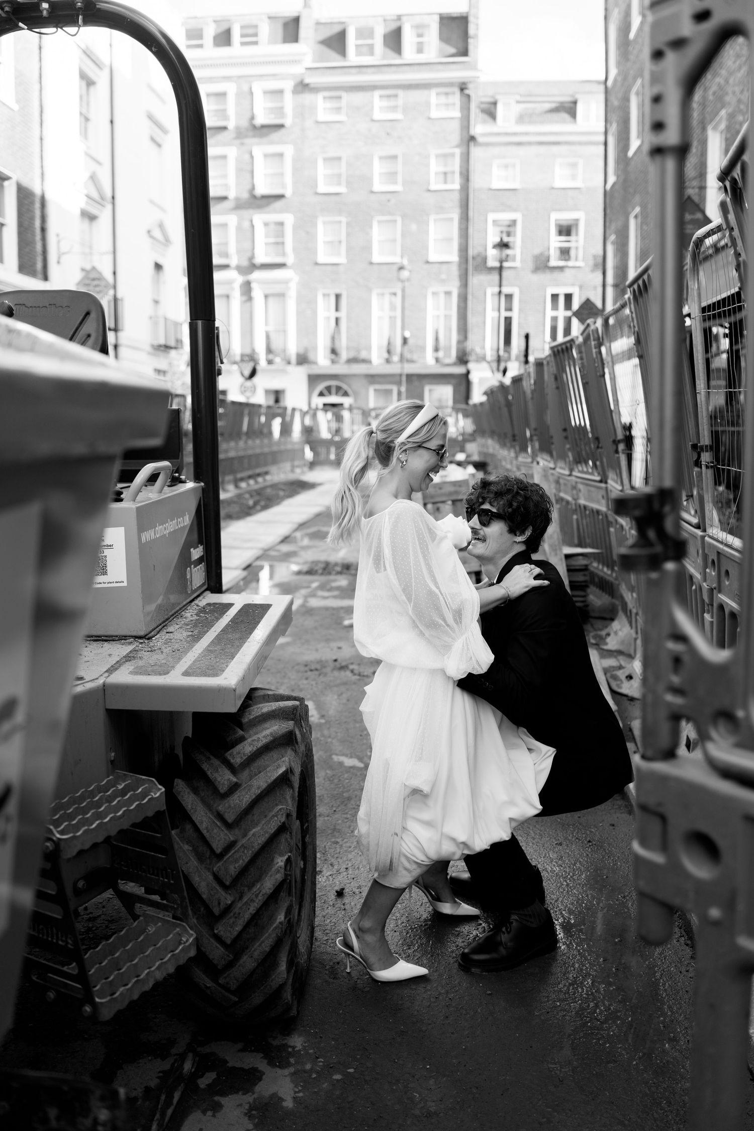 Wedding couple creates playful poses on a construction vehicle in an urban setting.