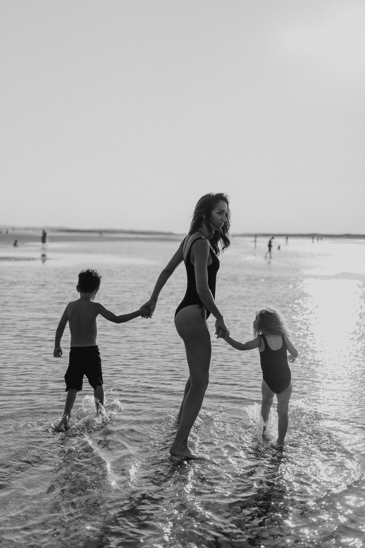 Black and white photo of people playing in ocean waves at a beach.