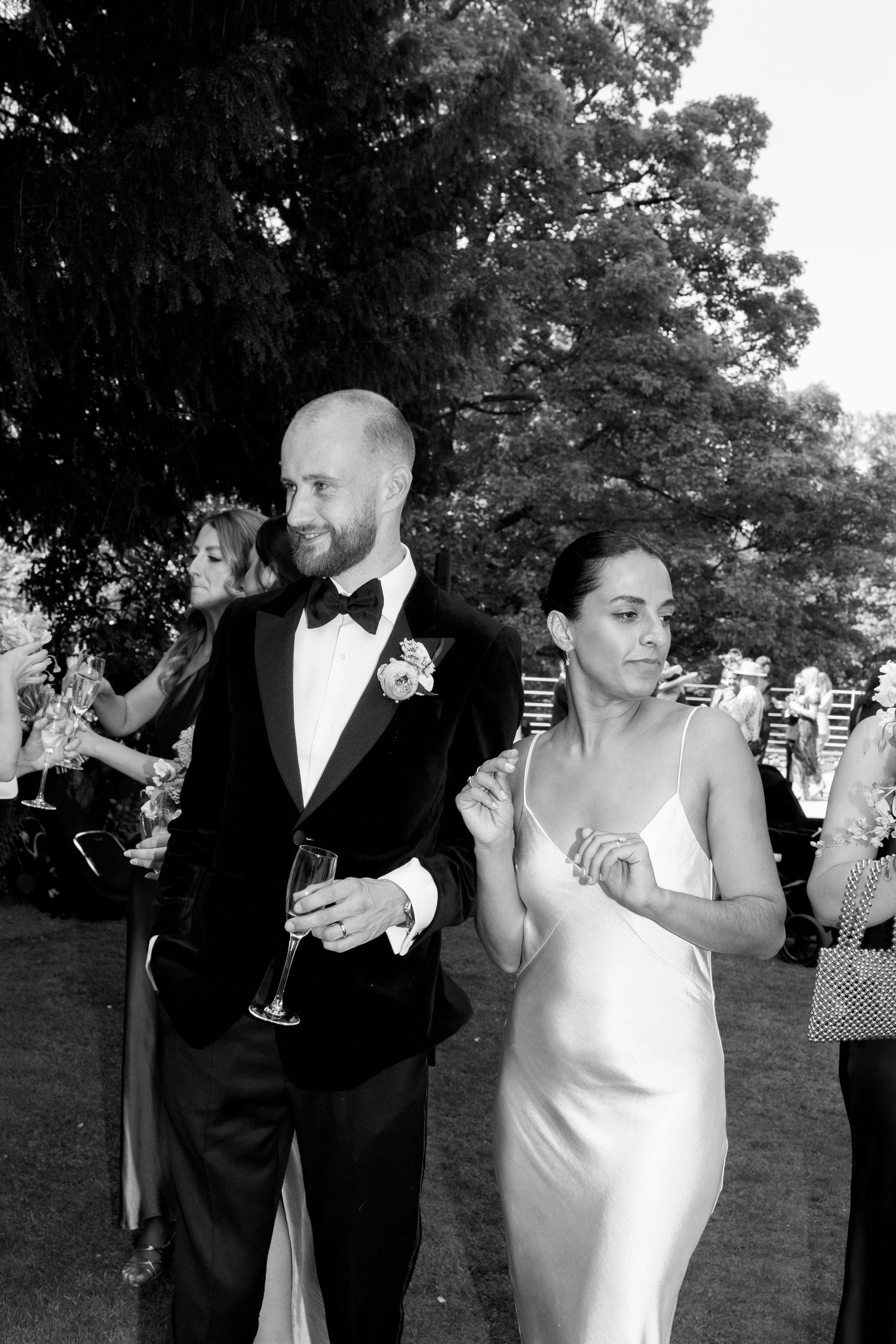 Wedding couple and guests raise champagne glasses for a celebratory toast outdoors.