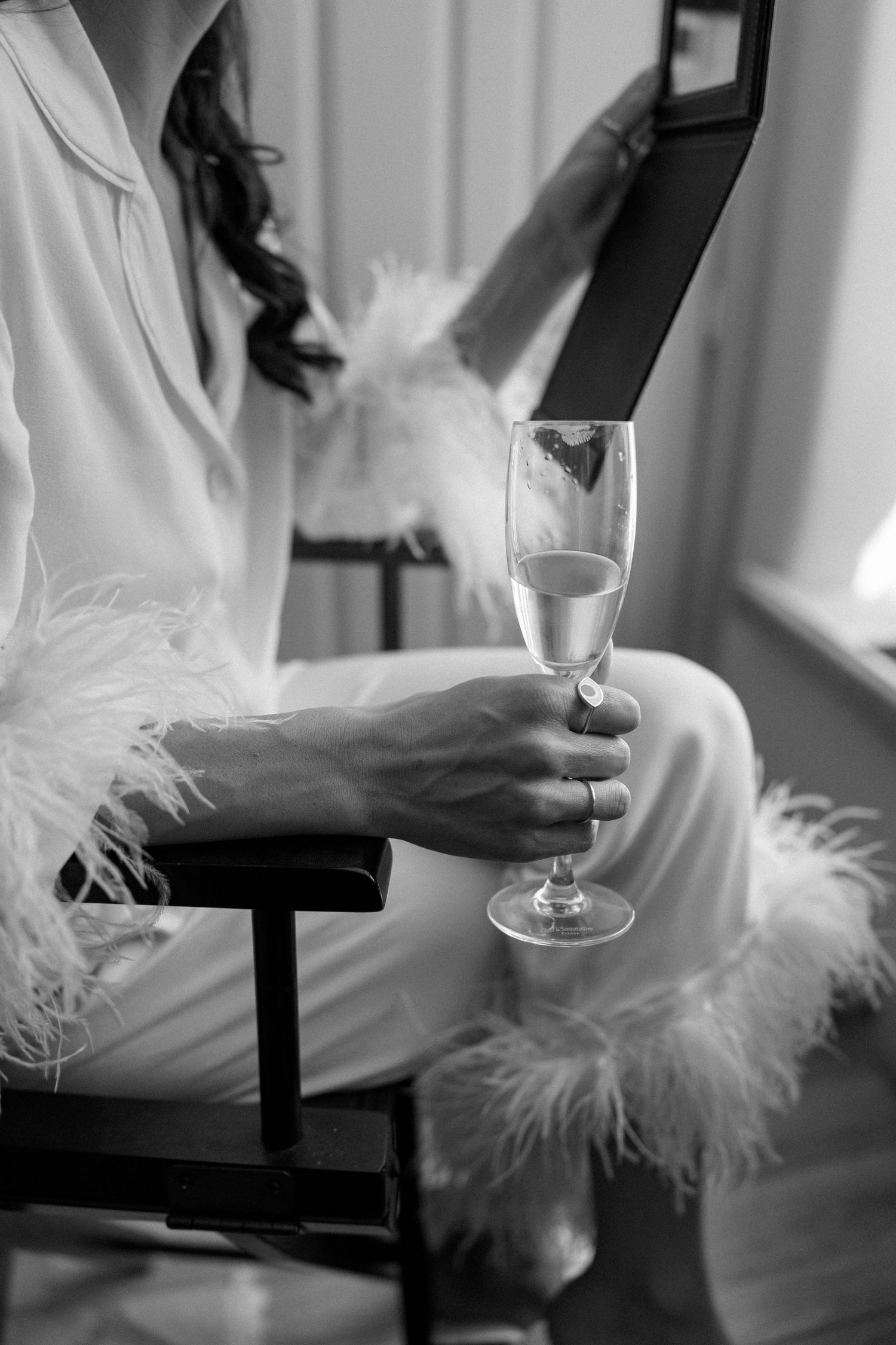 Person in white holding champagne glass with feather detail visible.