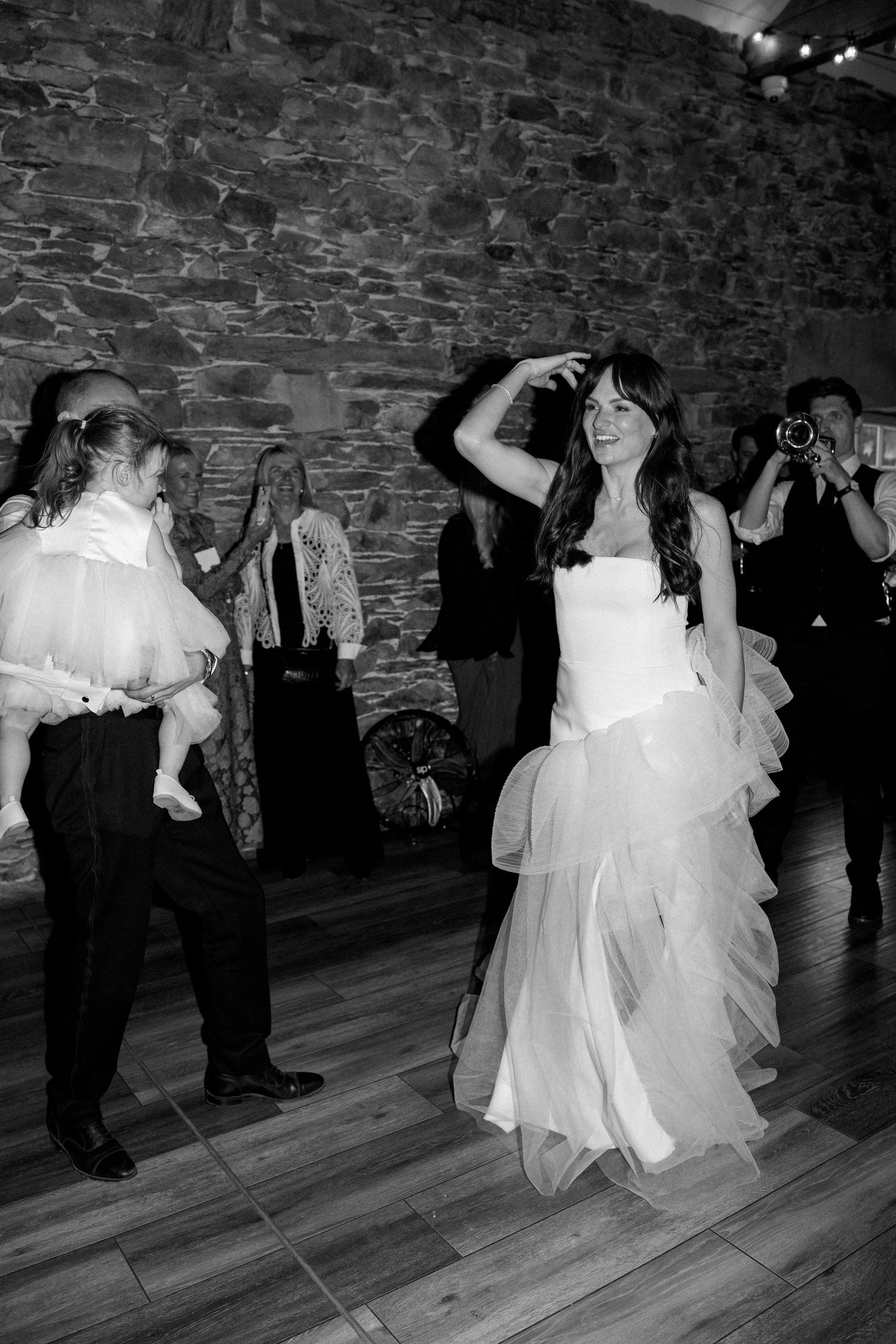 A bride in a flowing white gown dances joyfully in a rustic stone venue during her wedding reception.