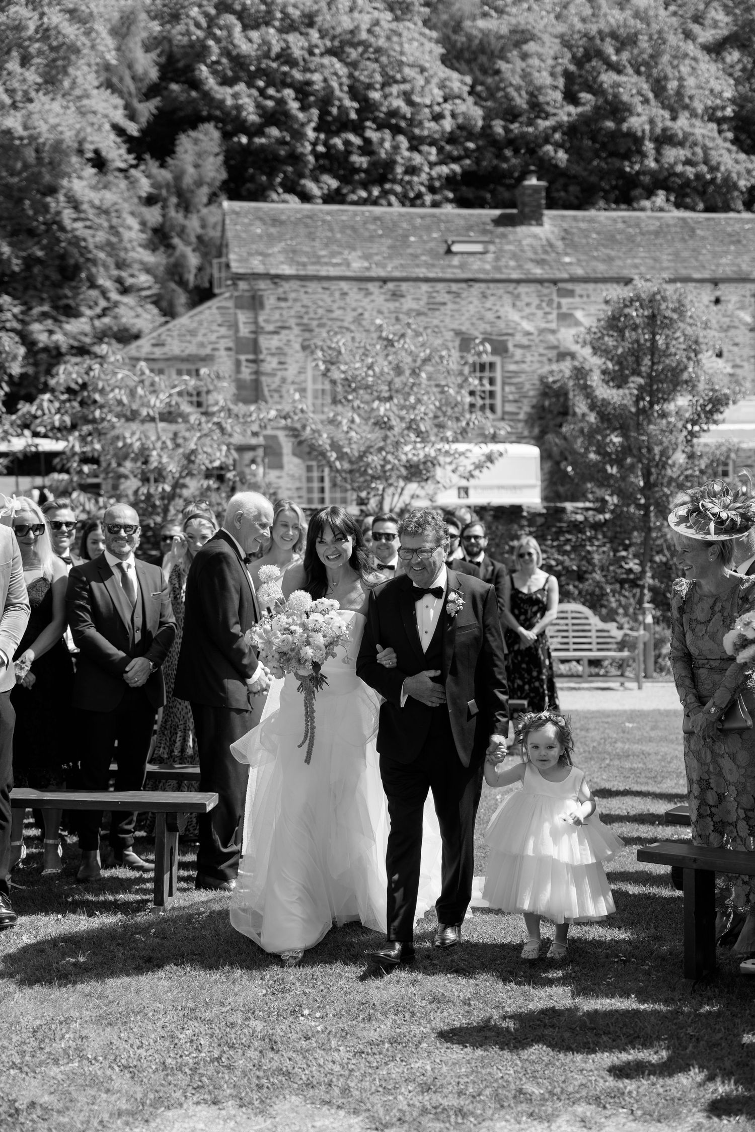 Black and white photo of wedding processional on garden grounds.