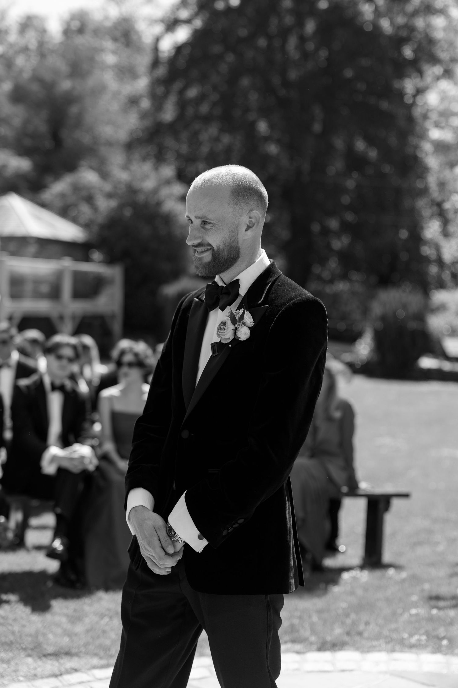 Wedding guests in formal attire gather on a sunny lawn during an outdoor celebration.