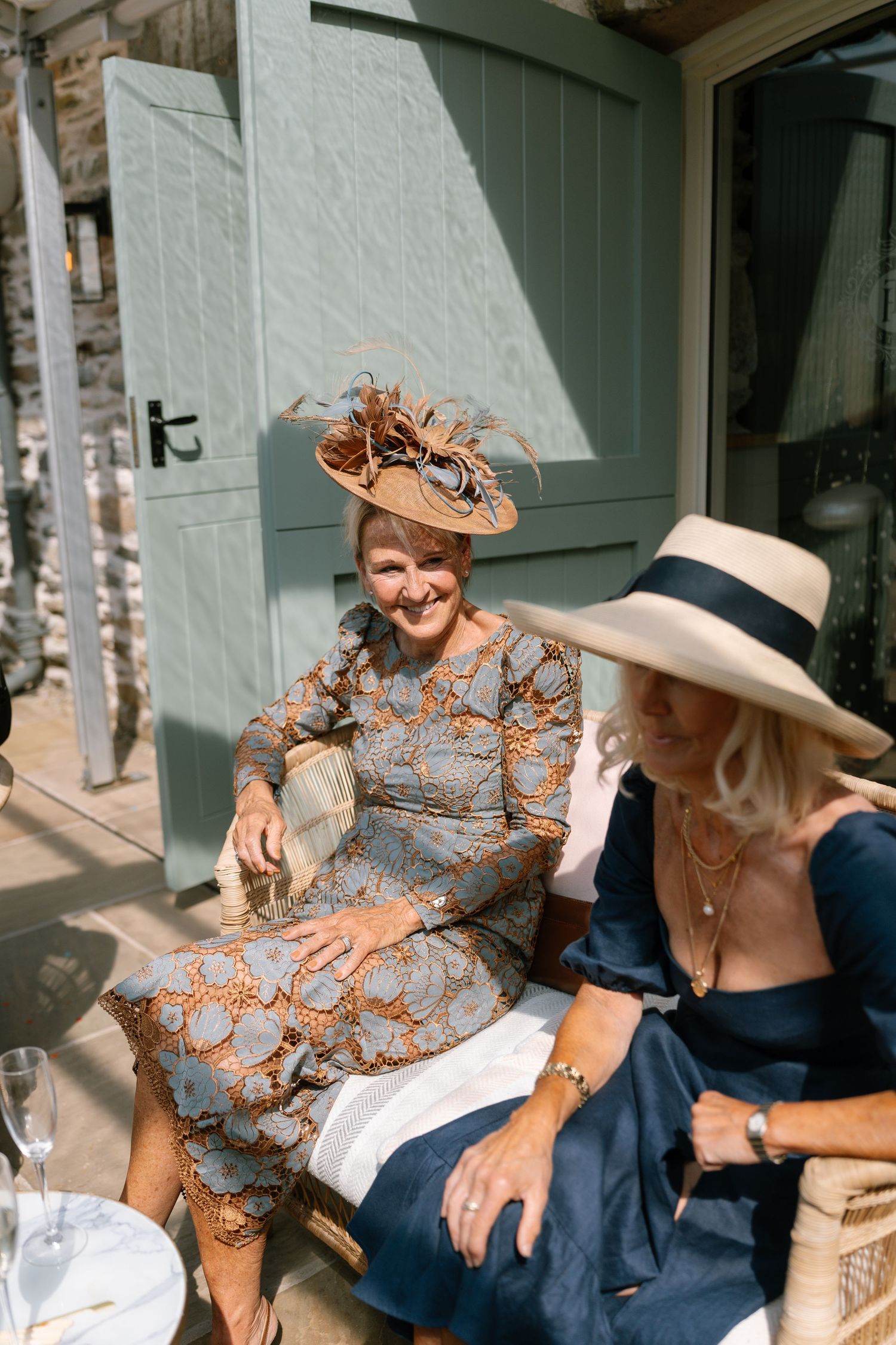 Guests in elegant attire and fancy hats socialize at an outdoor wedding reception.