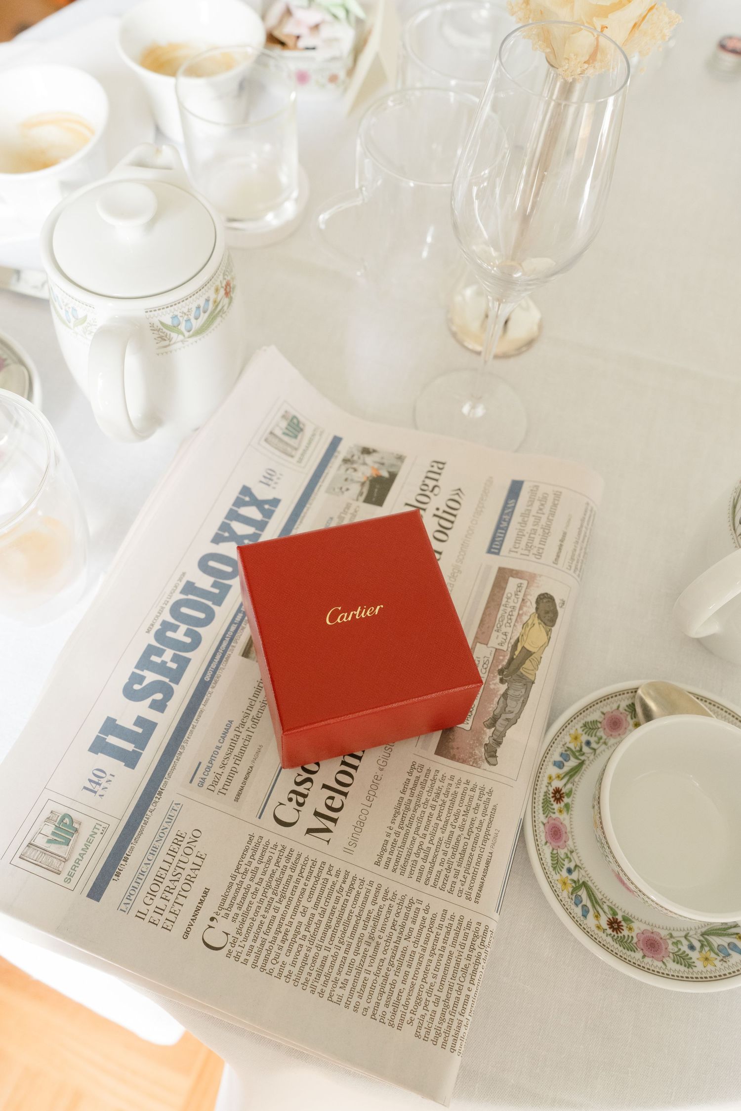 Red Cartier gift box on Italian newspaper Il Secolo XIX at an elegant table setting with fine china.