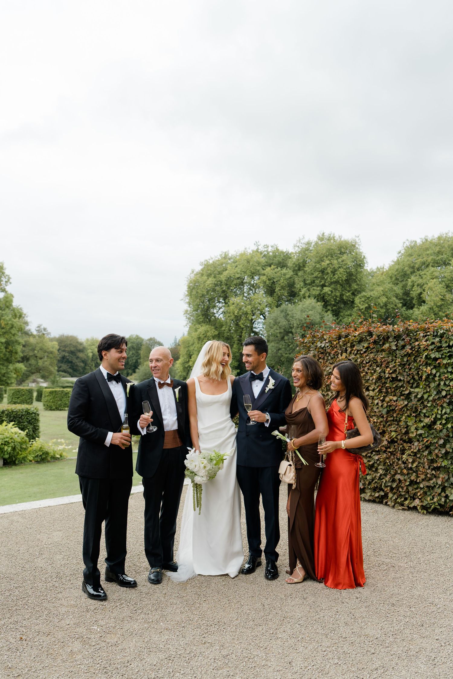 Bride and groom celebrate with wedding guests outdoors in formal attire at garden venue.