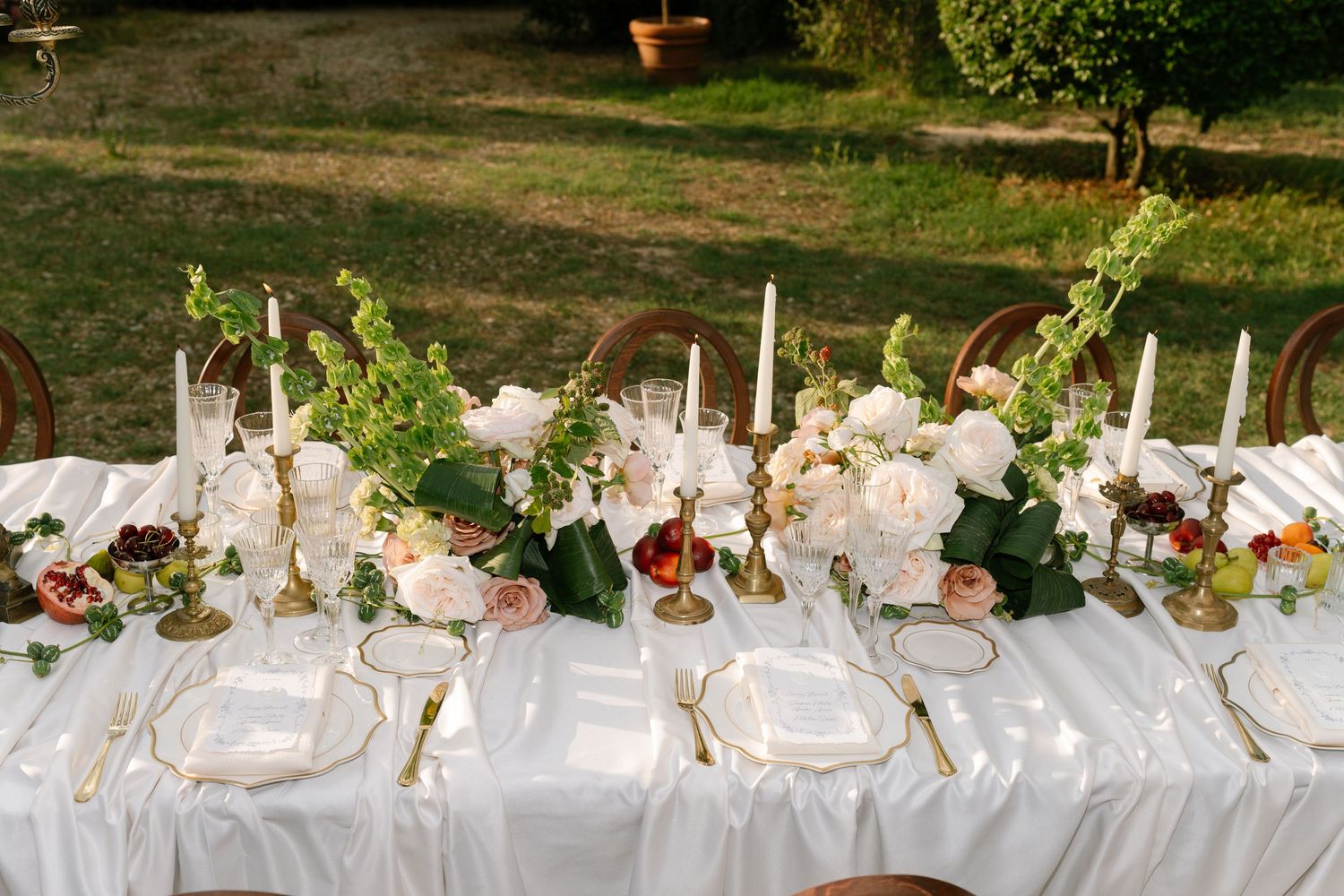 A long white-clothed banquet table set up outdoors for a wedding reception.