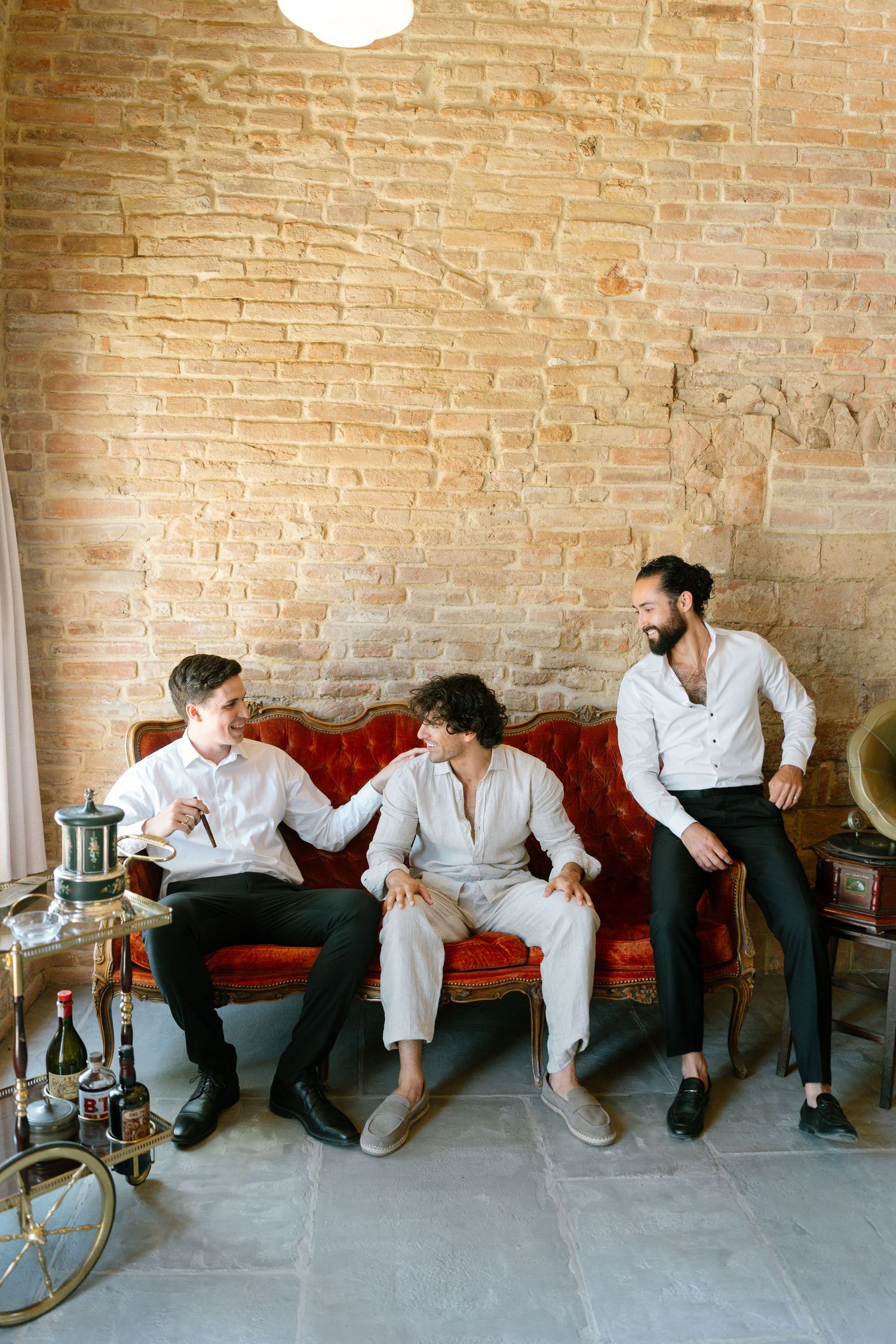 People in white attire lounging on red couches in a brick-walled room.