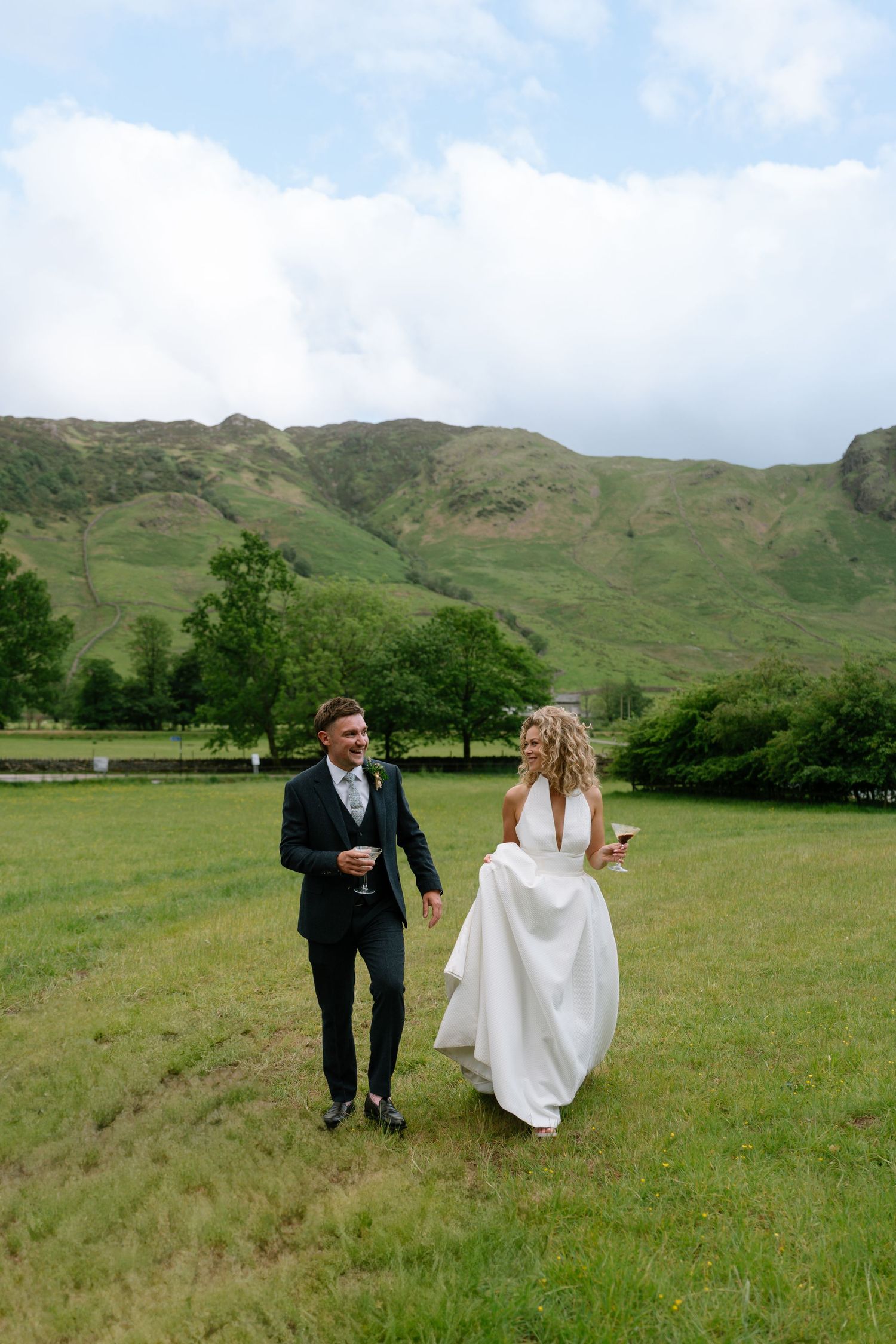 Newlyweds stroll through a scenic meadow with rolling hills in the Lake District.