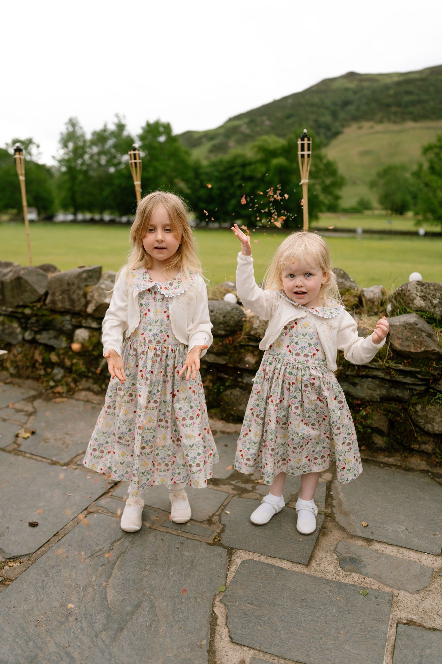 Two young girls in floral dresses pose together on a stone walkway.