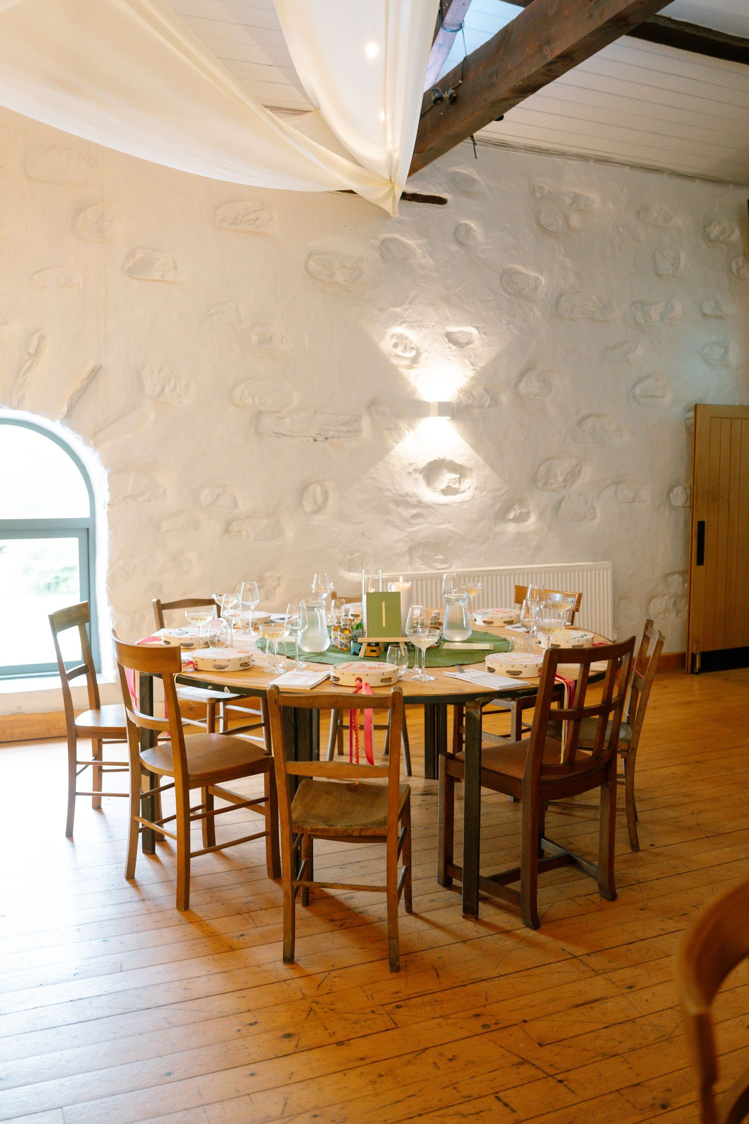 Rustic dining room setup with wooden chairs around a table under textured white walls and exposed beams.