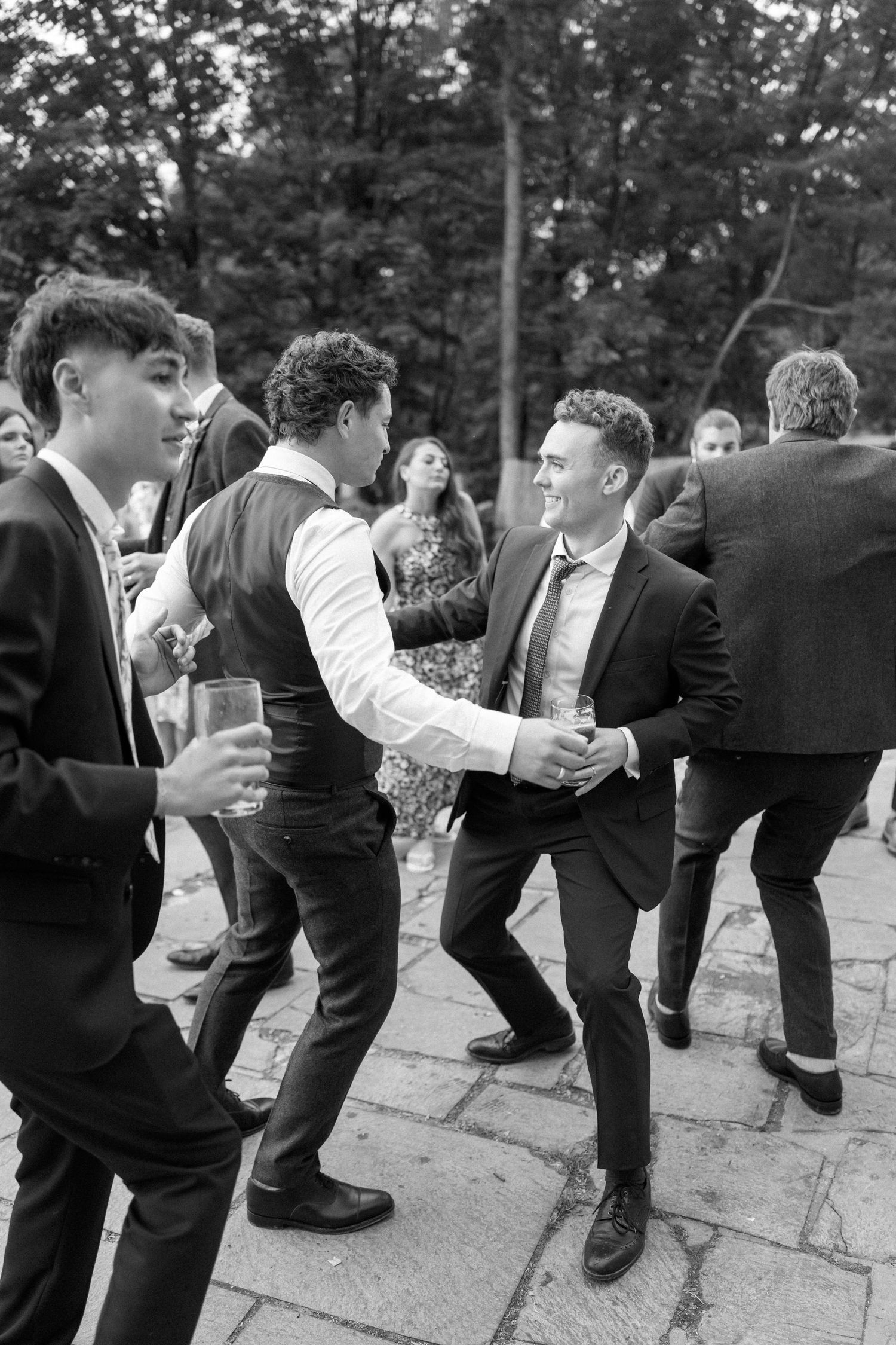 Black and white photo of wedding guests dancing in formal attire.