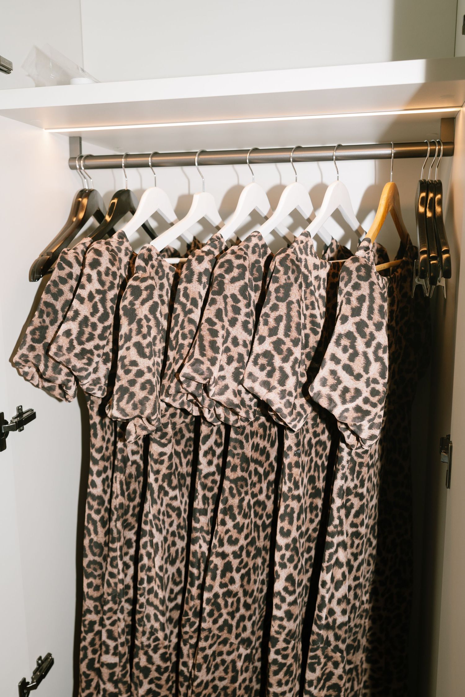 Multiple leopard print dresses hanging on wooden hangers in a closet.