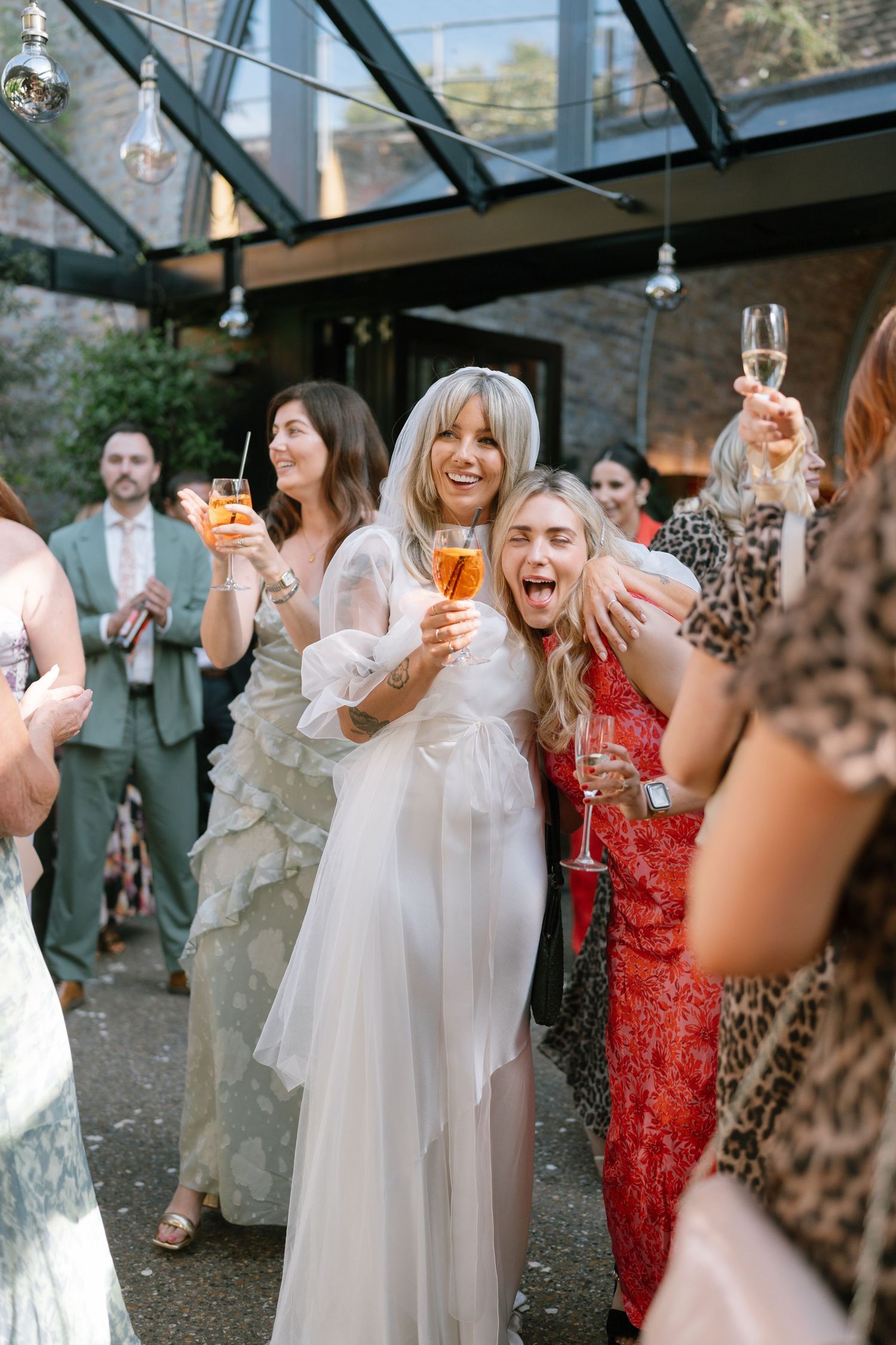 Wedding celebration under a glass ceiling with guests raising champagne glasses in celebration.