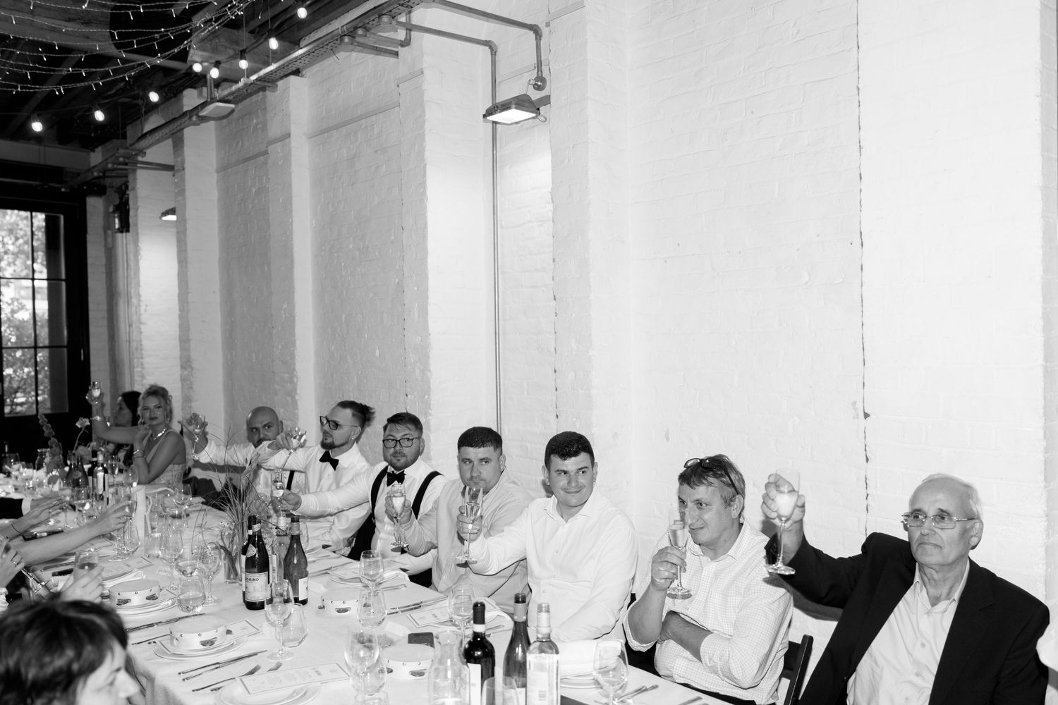 Wedding reception dinner in a bright white industrial space with guests seated at long tables.