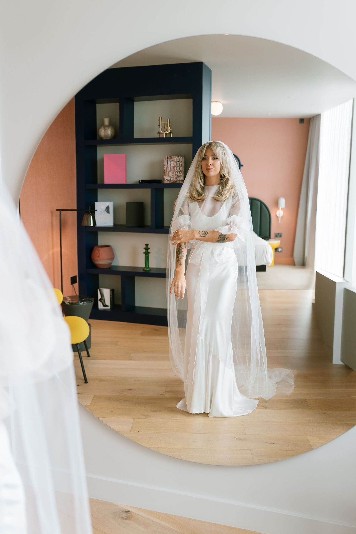 Wedding preparation scene in modern room with white dress and mirror reflections.