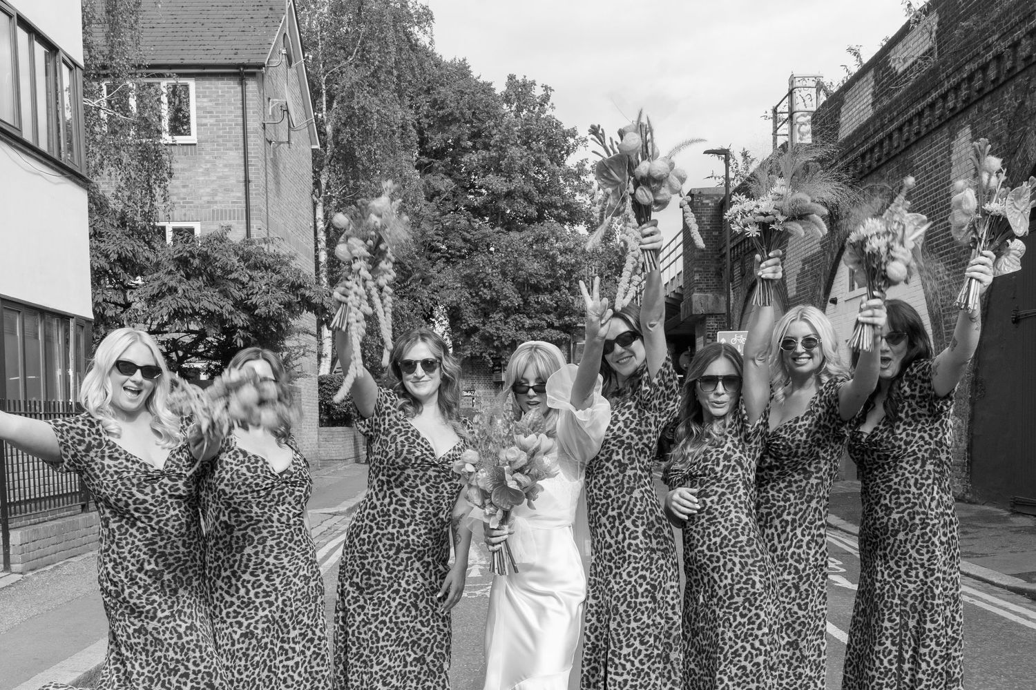 Wedding party in black and white poses together outdoors with coordinated leopard print outfits.