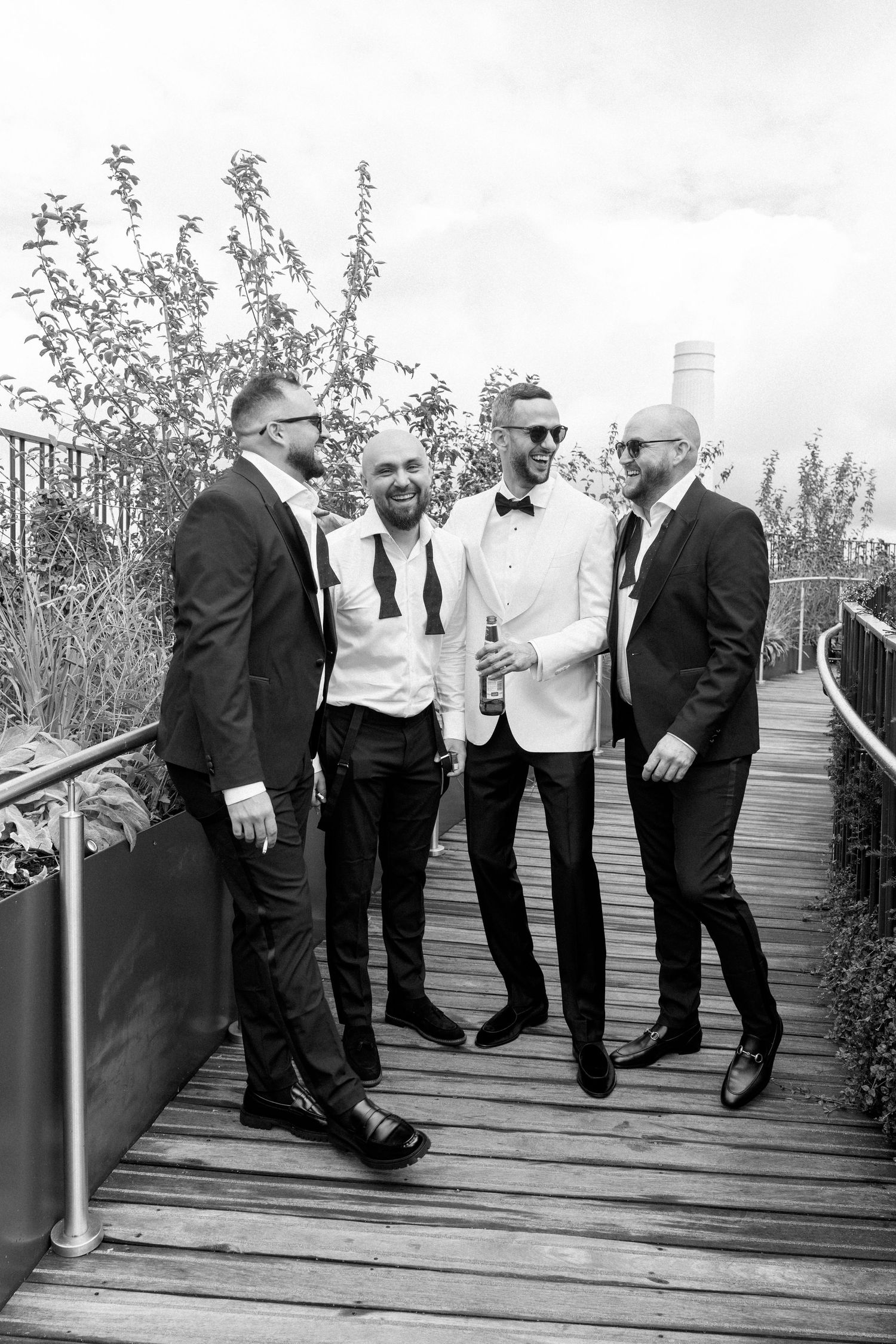 Wedding party members in formal attire share candid moments on a wooden deck.
