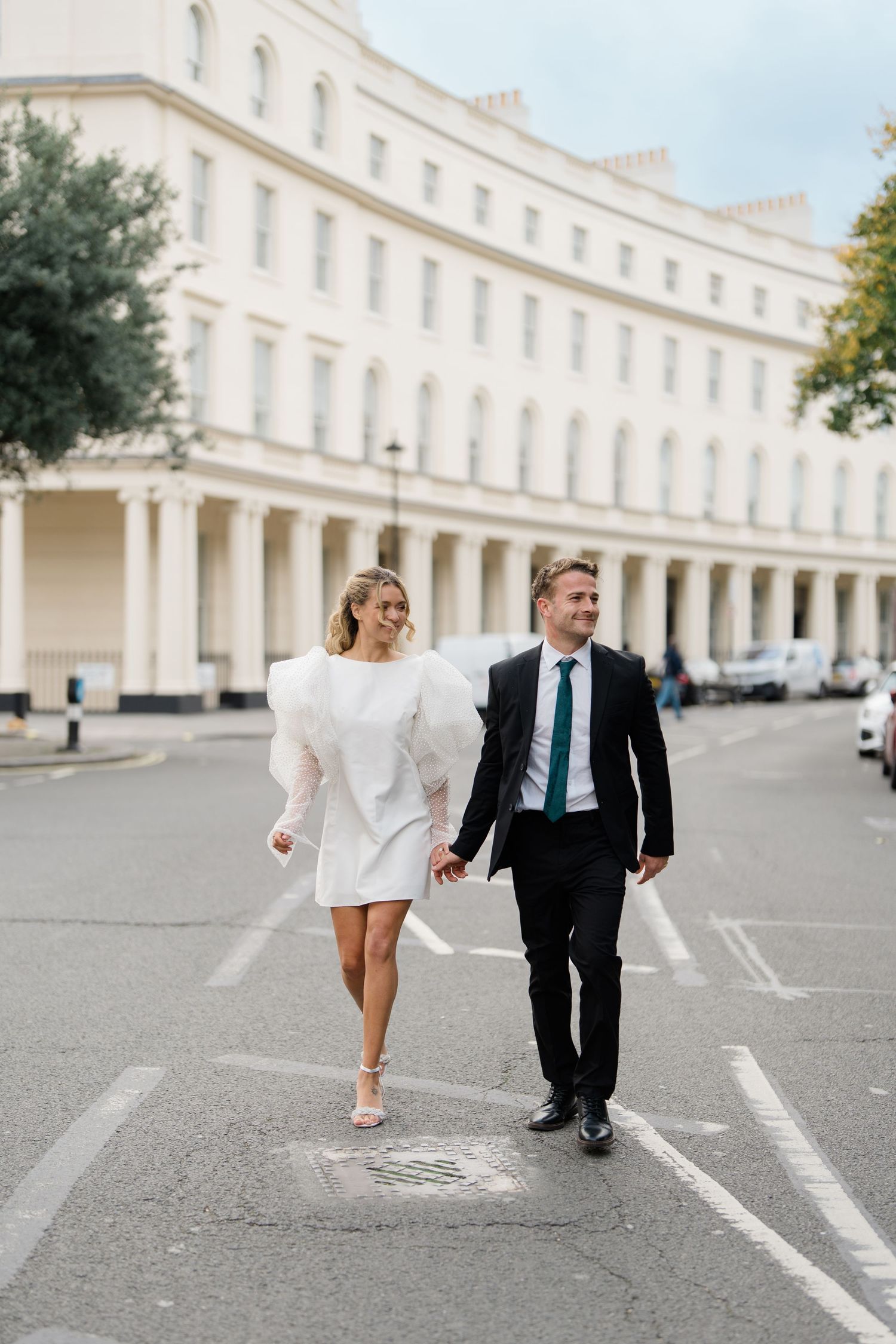 A couple walks playfully along a grand historic colonnade with white pillars and architecture.