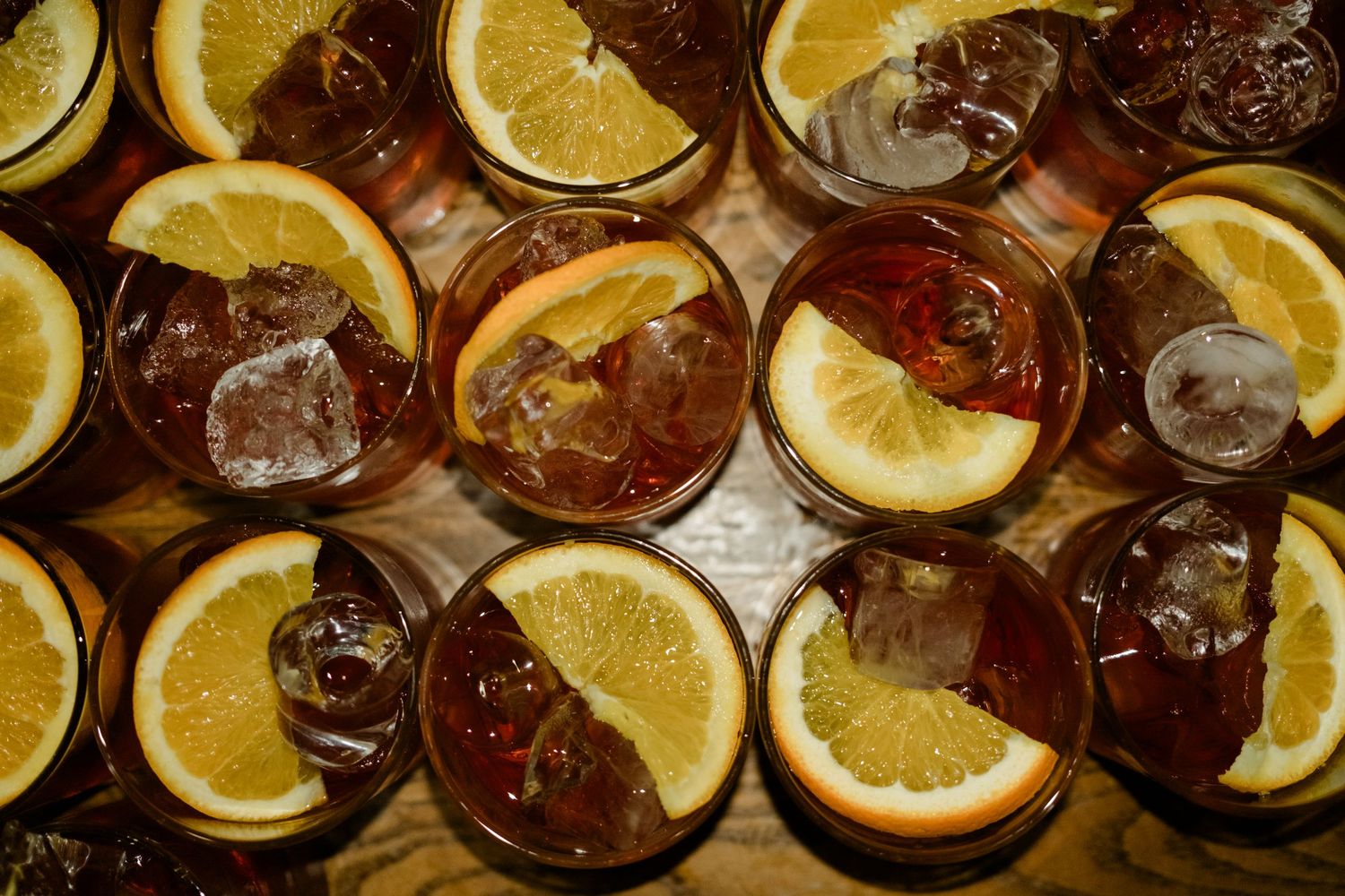 Overhead view of cocktails garnished with orange slices and ice cubes in multiple glasses.