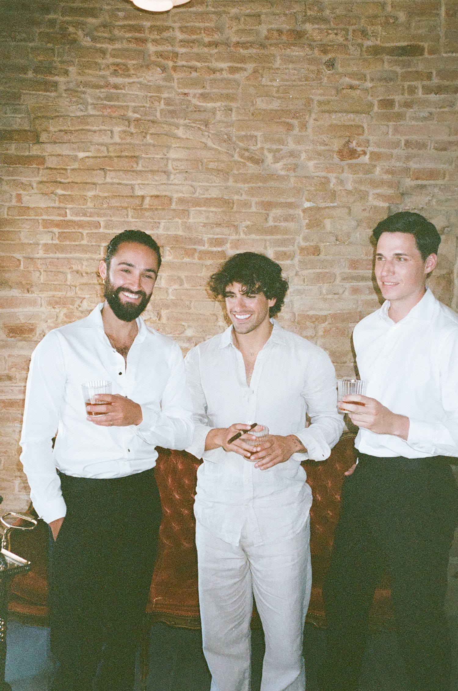 A group in white shirts and dark pants stand against a brick wall at what appears to be a social gathering.