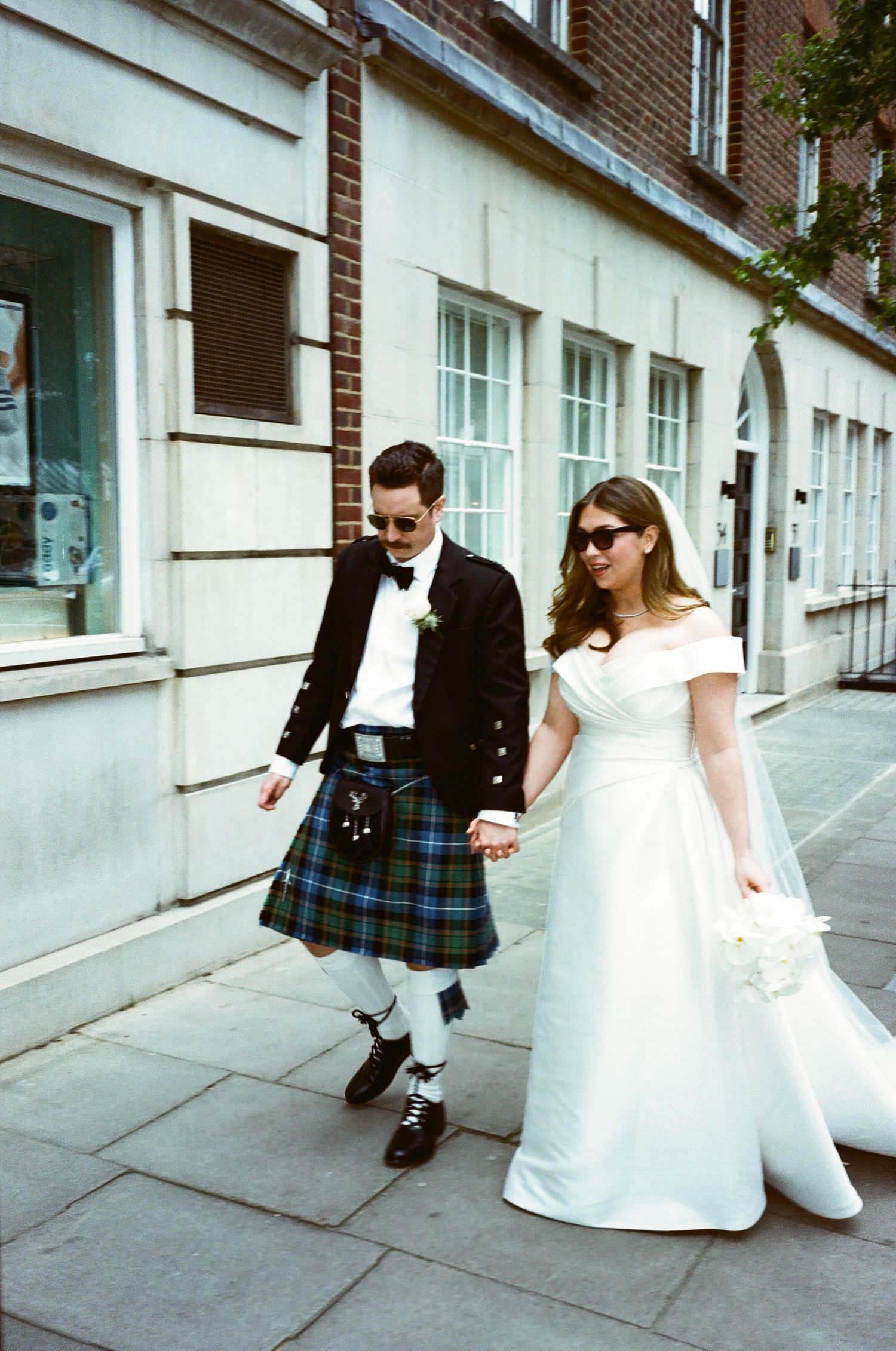 A wedding couple playfully poses in a sequence of four artistic photos along a brick building exterior.