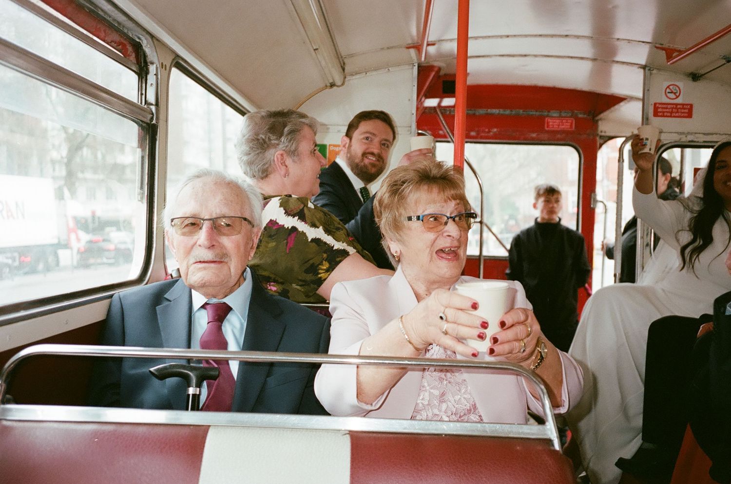 Passengers seated inside a public transit bus with red interior details and large windows.