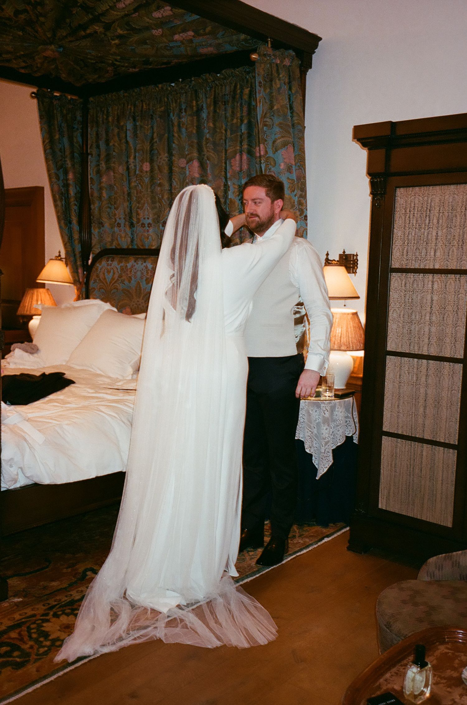 A couple shares a tender moment in a bedroom with an ornate canopy bed and vintage decor.
