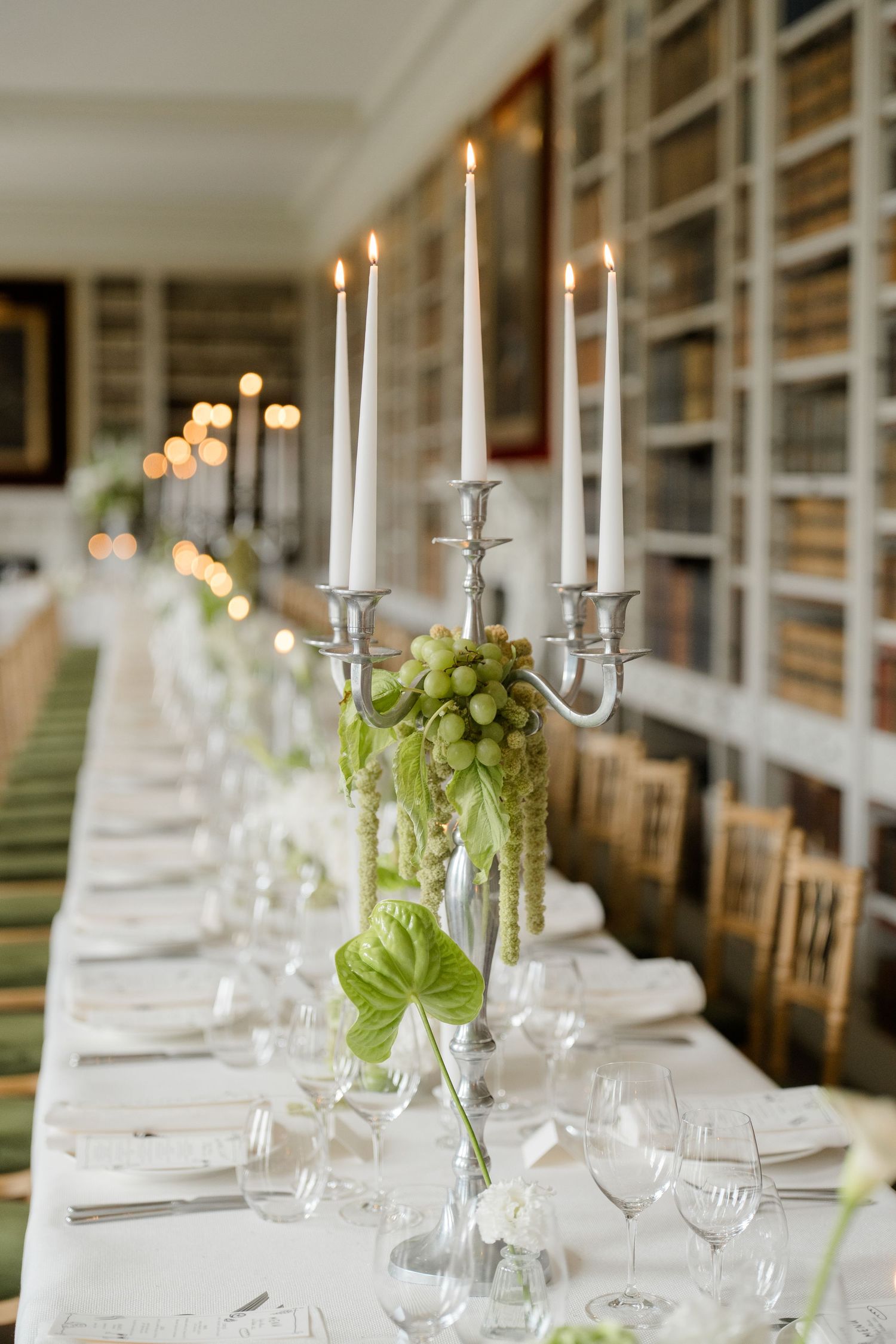 Elegant wedding reception table with silver candelabras and green grape decor in a library.