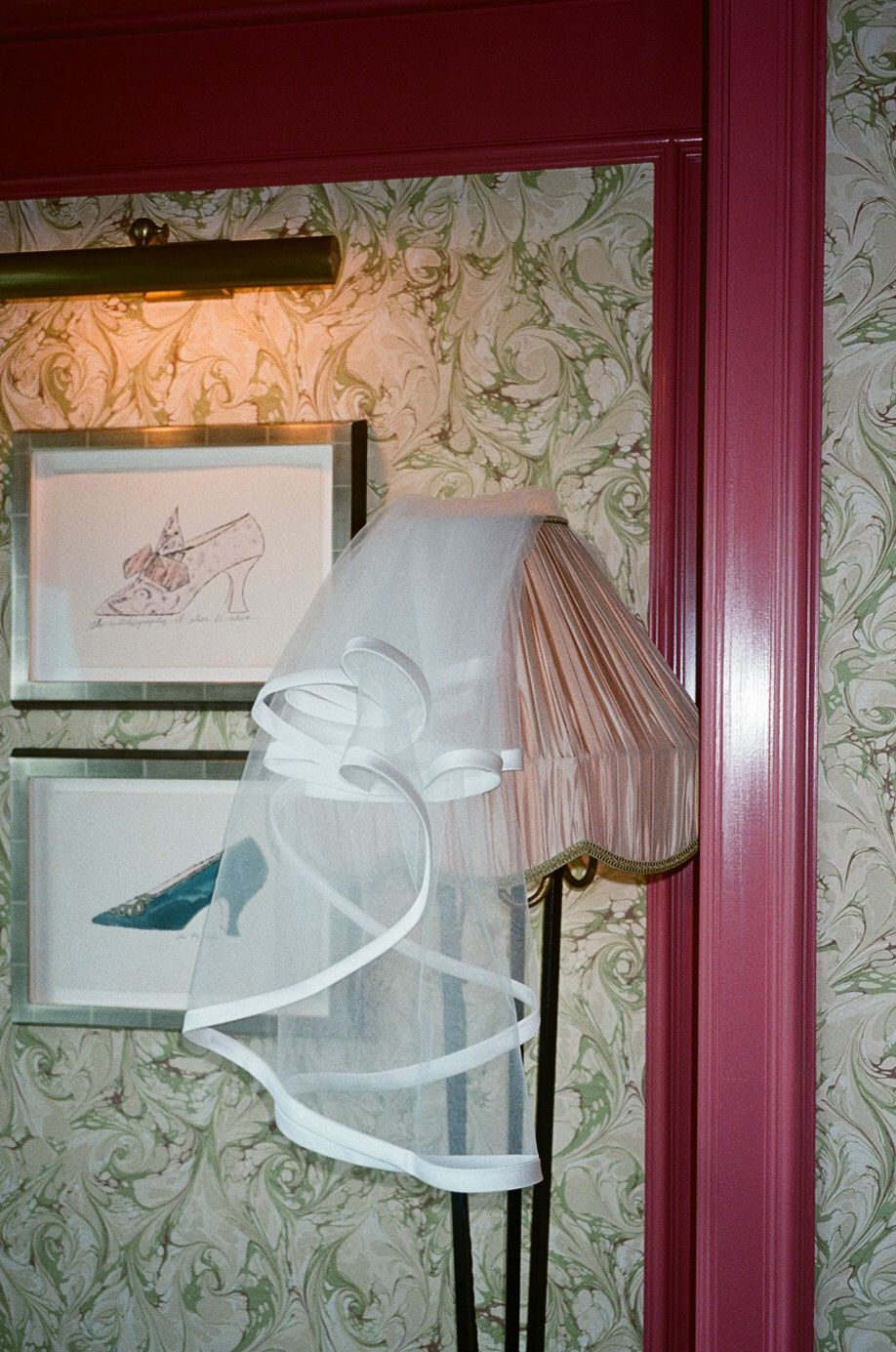 White wedding veil with ribbon trim draped over lamp in floral wallpapered room.