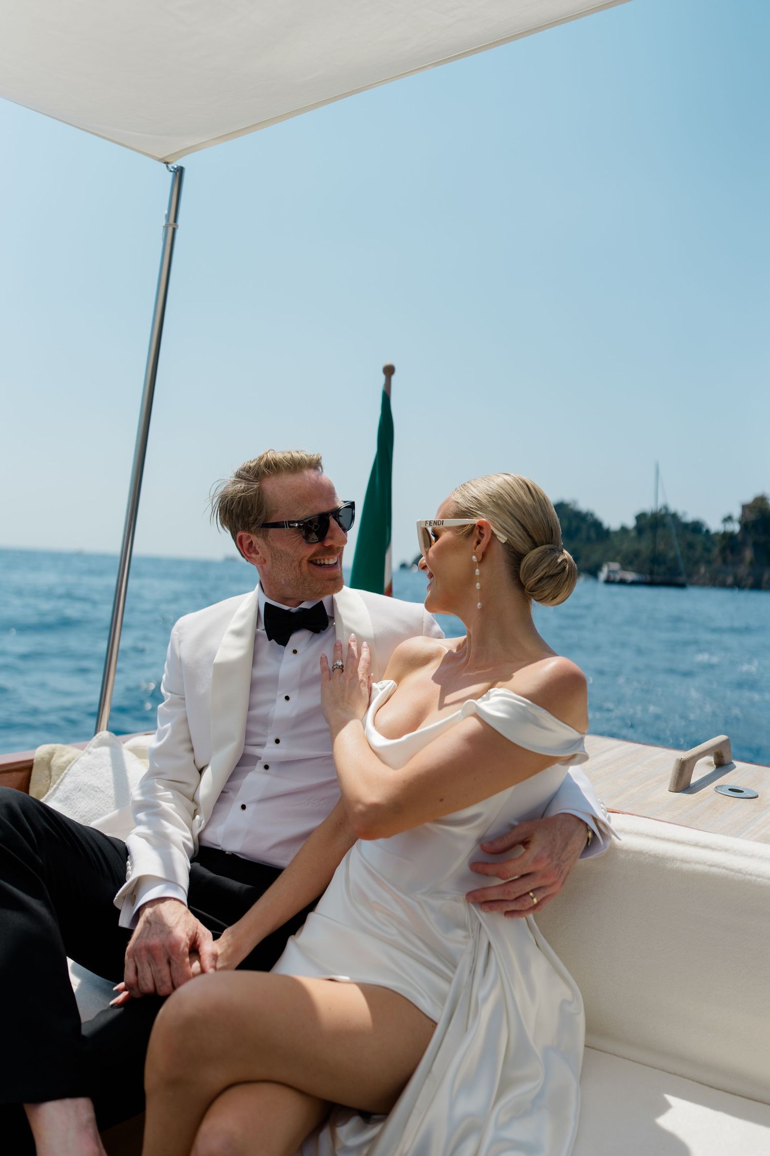 Elegant bride and groom in wedding attire sitting on a luxury boat on a sunny day.