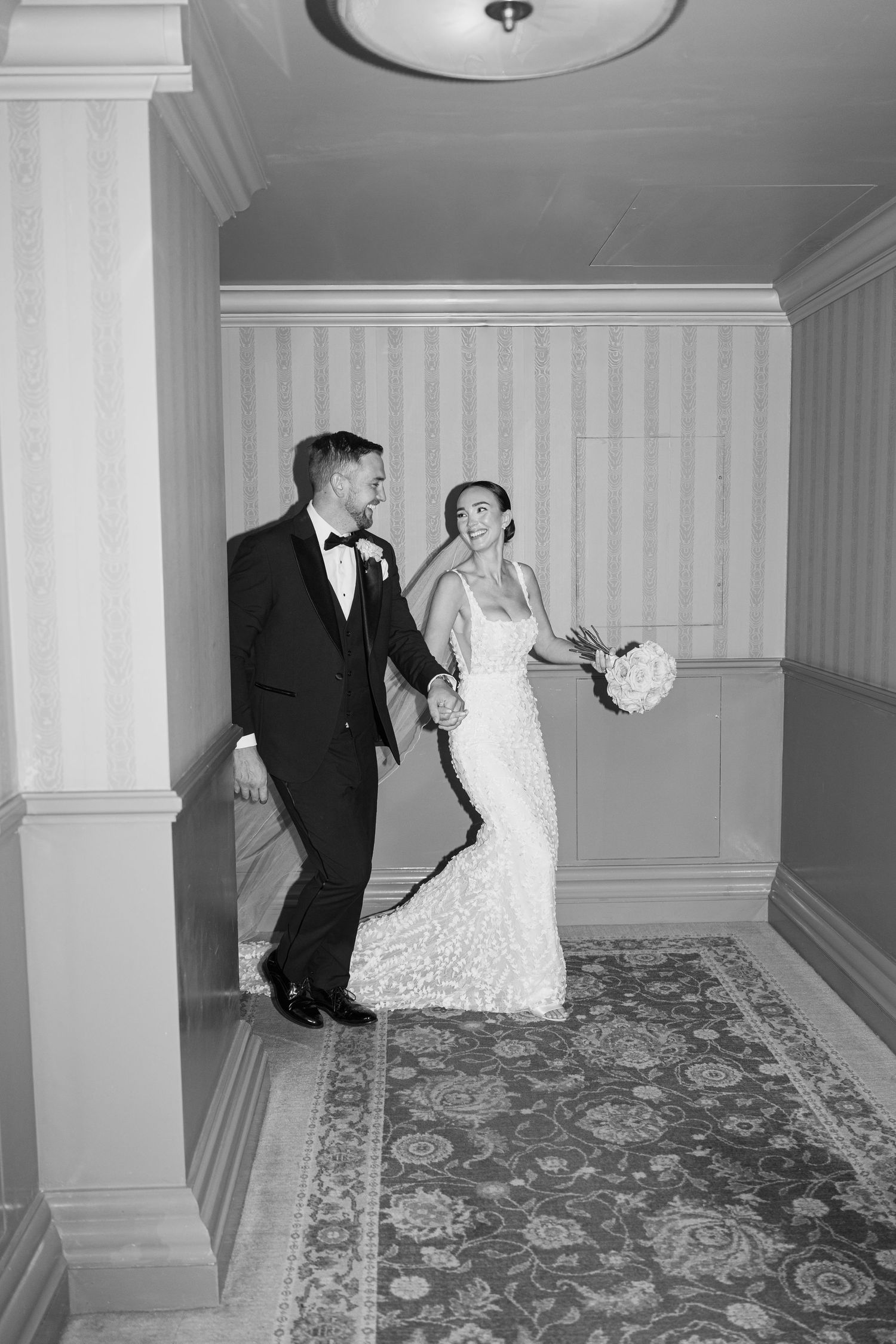 Newlyweds share intimate moments in elegant hotel corridor.