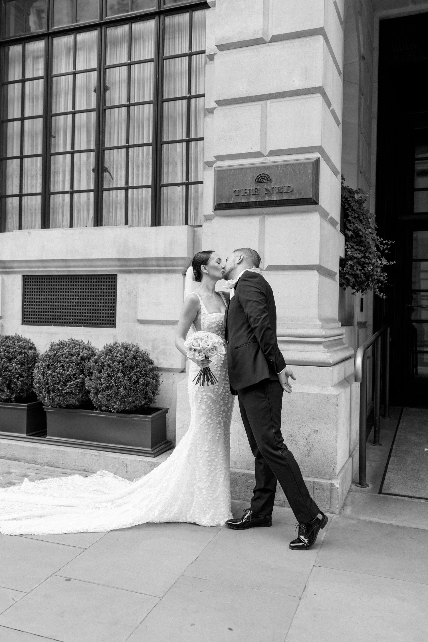 A romantic black and white wedding moment captured outside a historic building with decorative architecture.