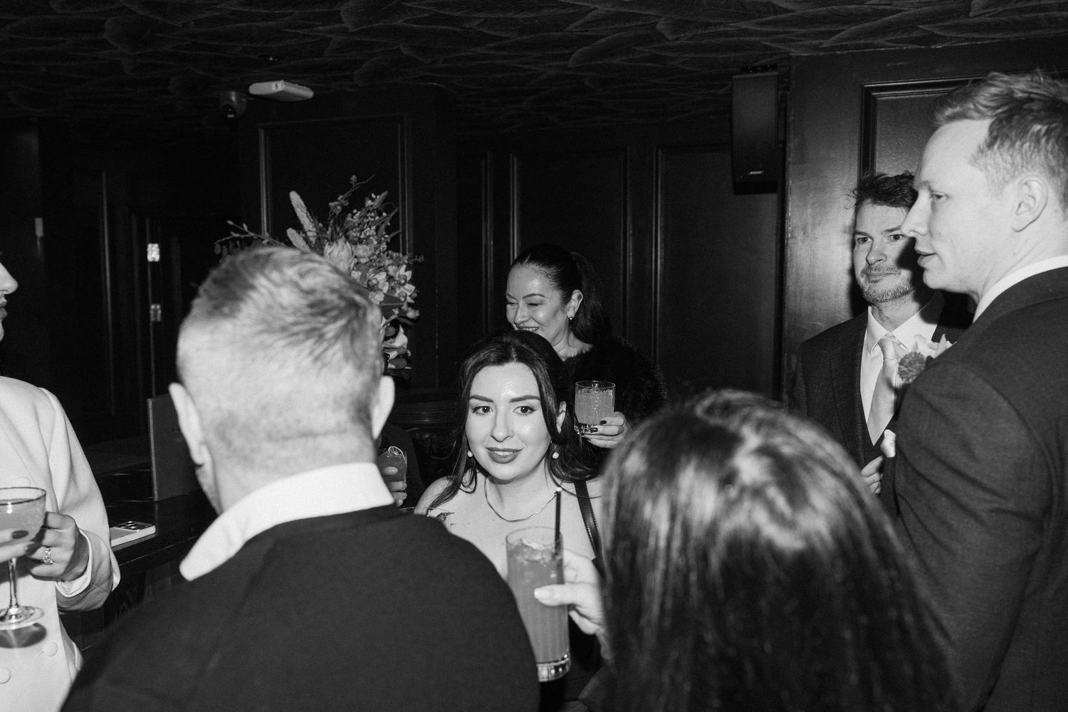 Black and white candid photo of wedding guests mingling and socializing at elegant reception.