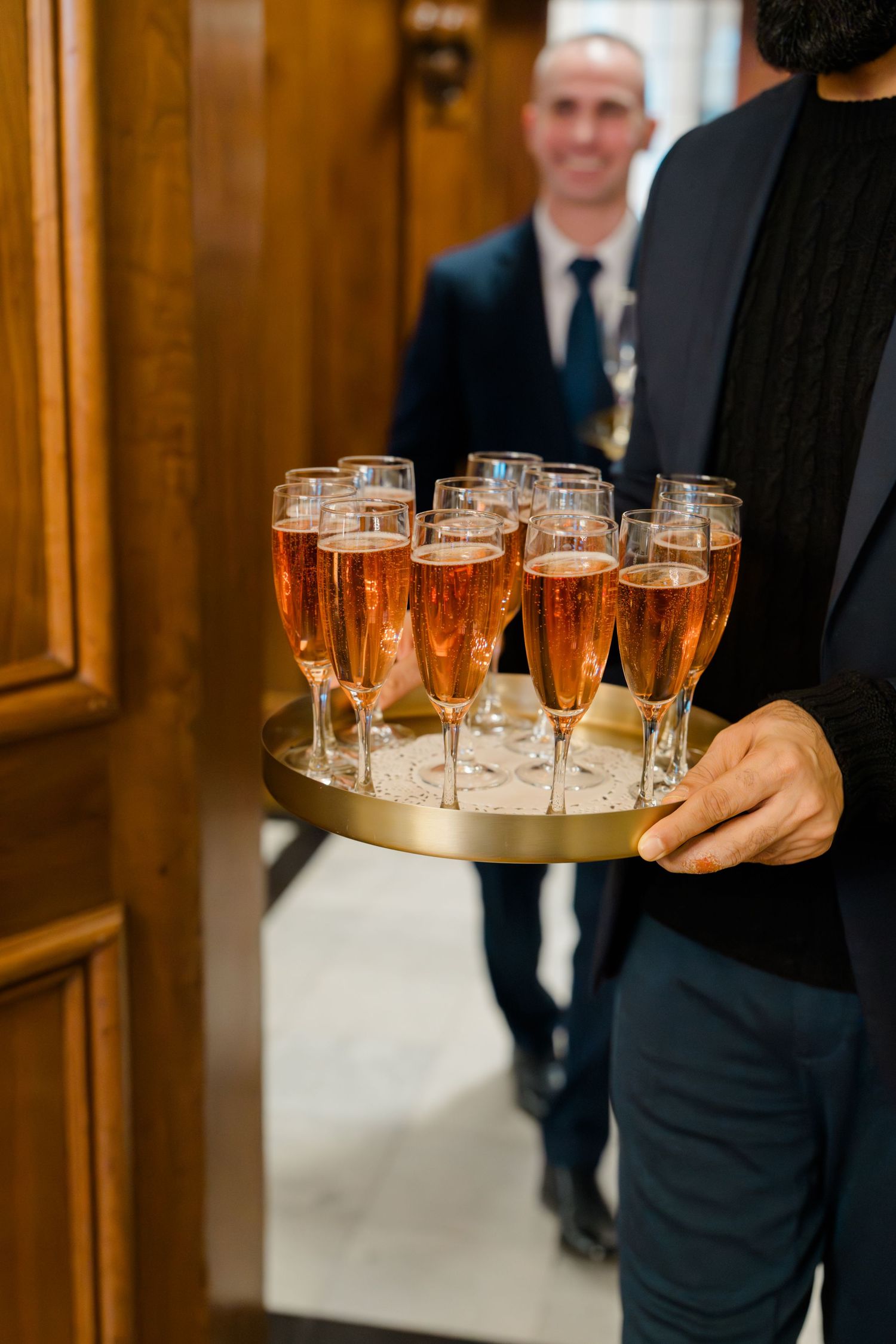 Server holding gold tray of rose champagne flutes at wedding reception.