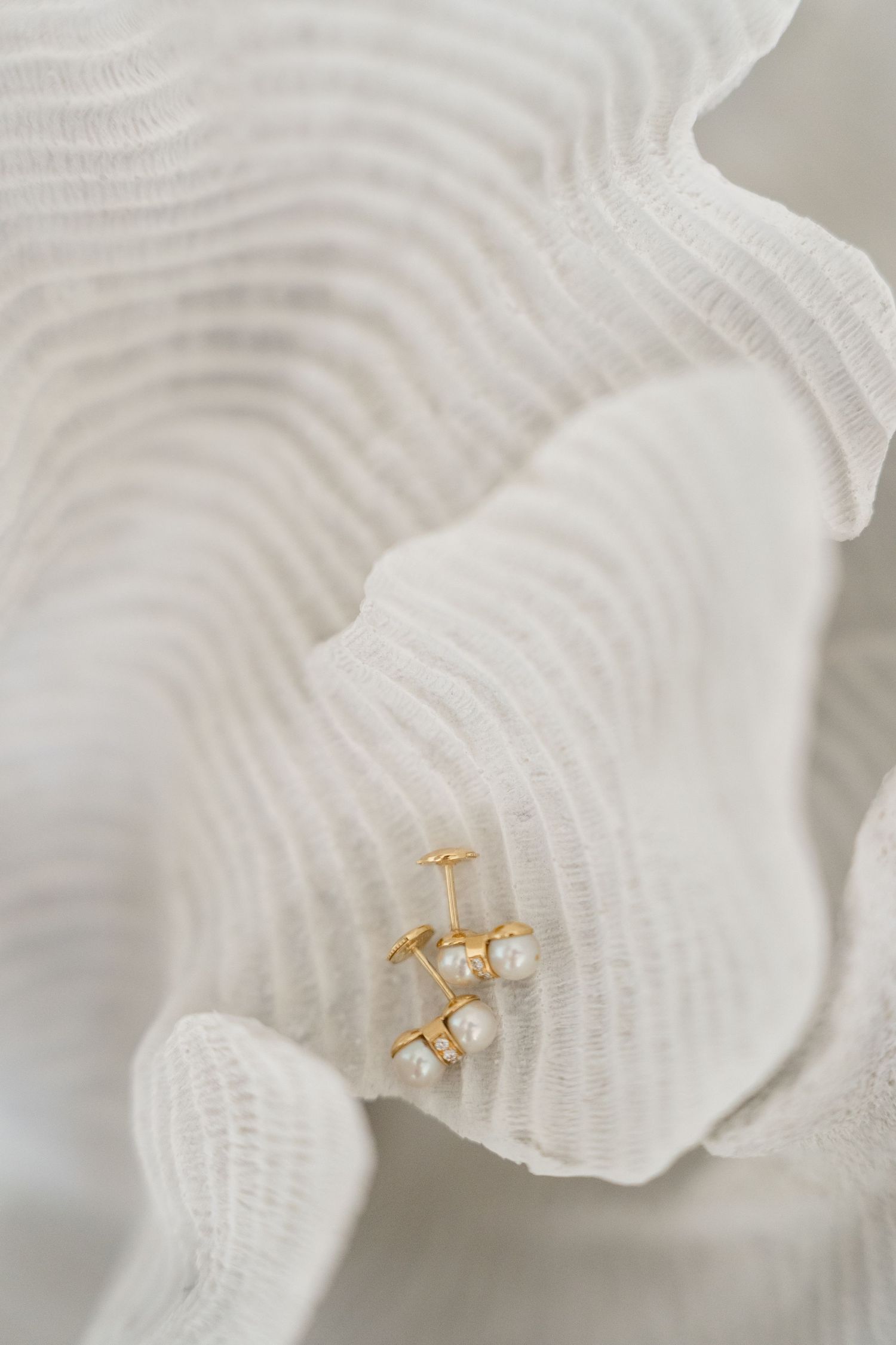Gold pearl stud earrings resting delicately on a white textured ruffled fabric surface.