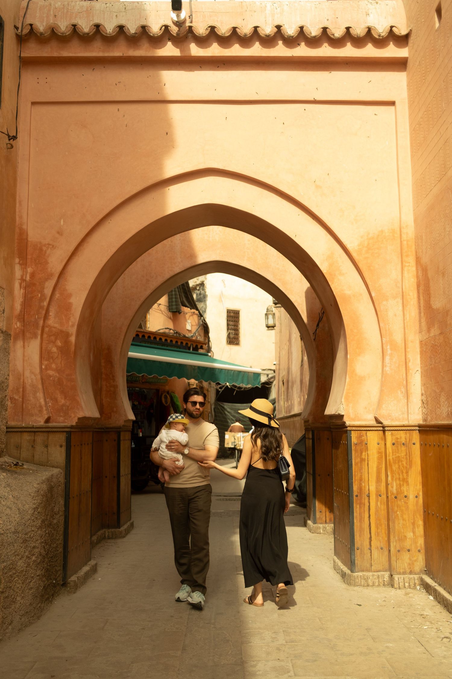 Couple with baby walking through ornate Moroccan archway in terracotta medina, Fez, Morocco.