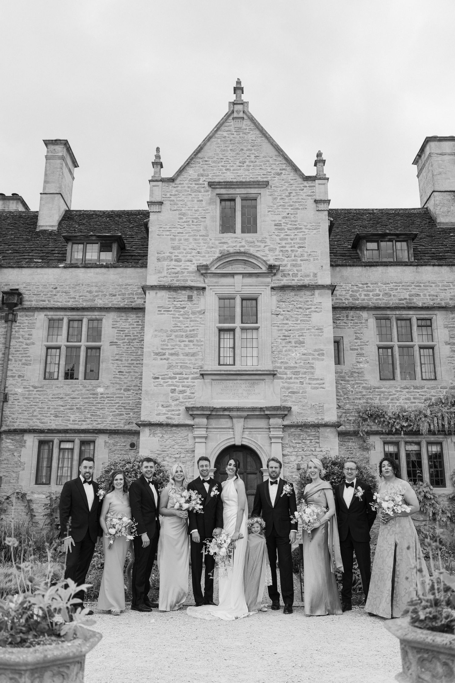 Wedding party poses in black and white photo before grand stone manor house facade.