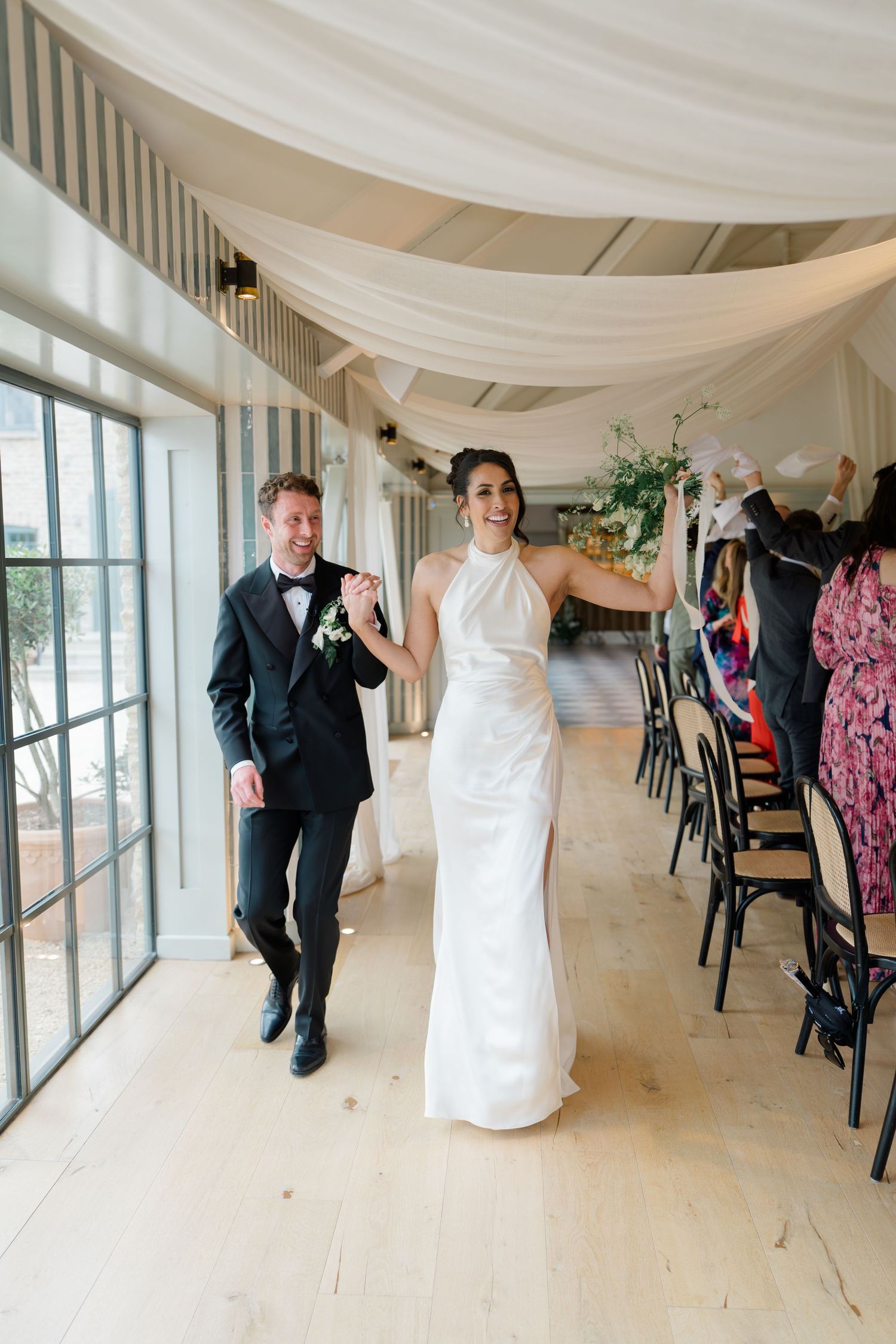 Bride in white halter gown and groom in tuxedo make grand entrance into draped wedding reception.